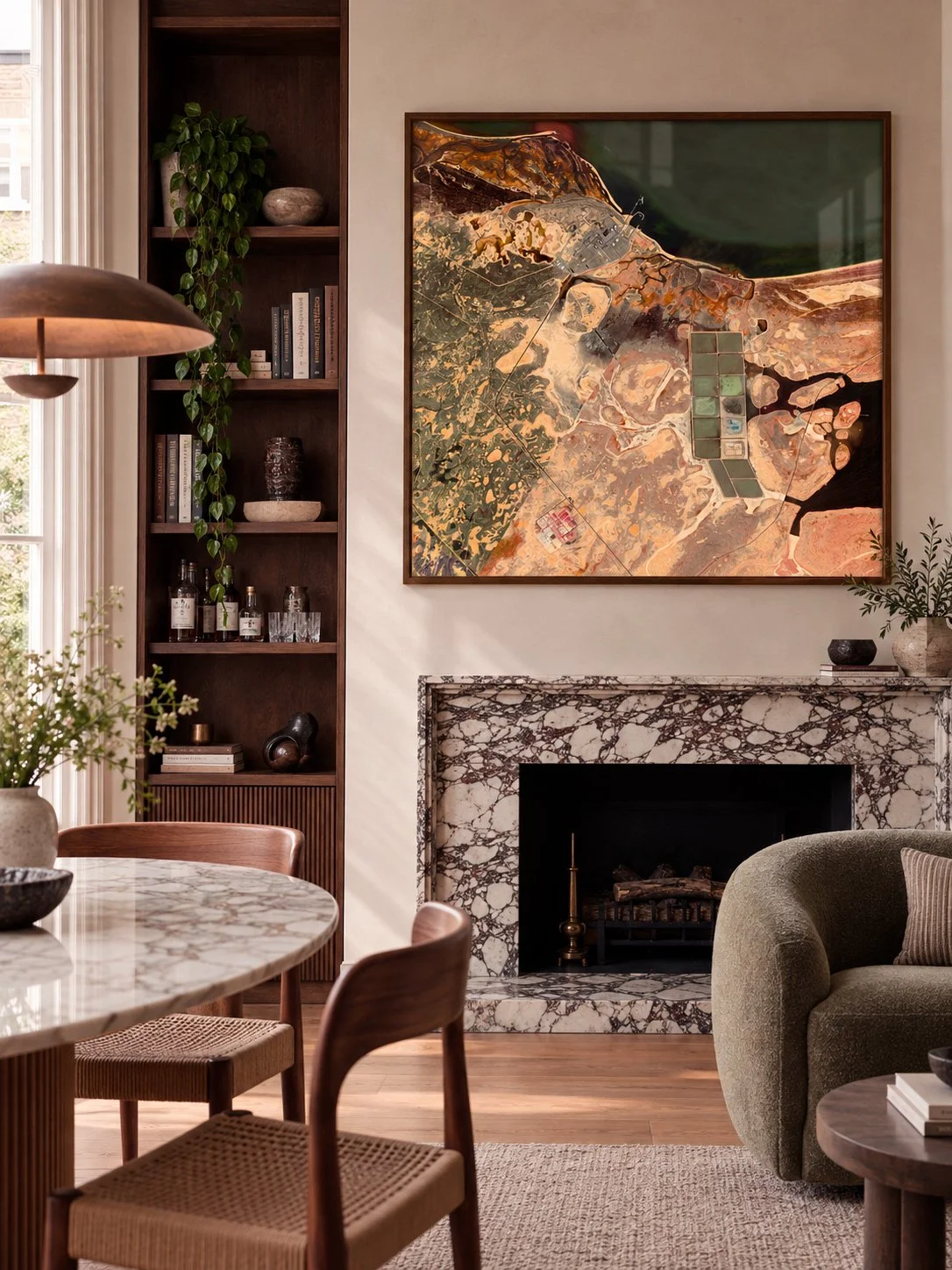 Living room with abstract art on the wall, marble fireplace, green armchair, wooden dining table with chairs, and built-in bookshelf with decorative items and books.