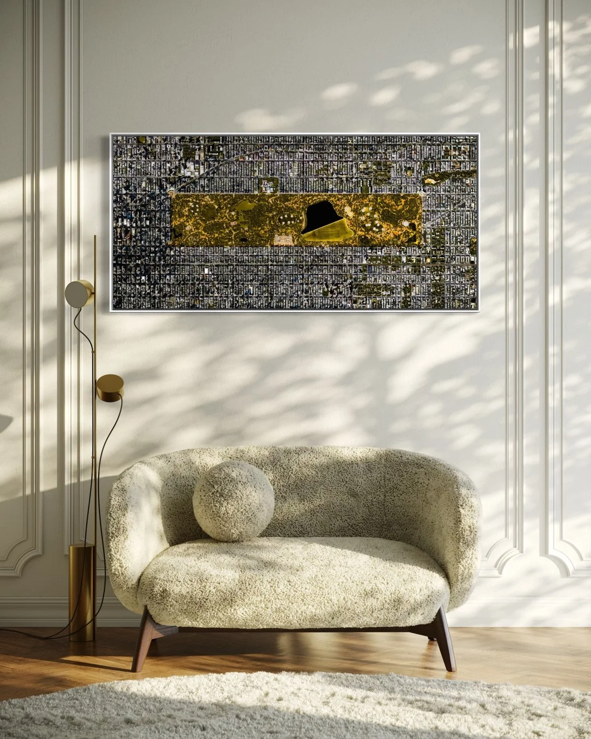 A living room with a textured beige sofa, a round beige pillow, a tall floor lamp, a framed city map, and sunlight creating shadows on the wall and hardwood floor.