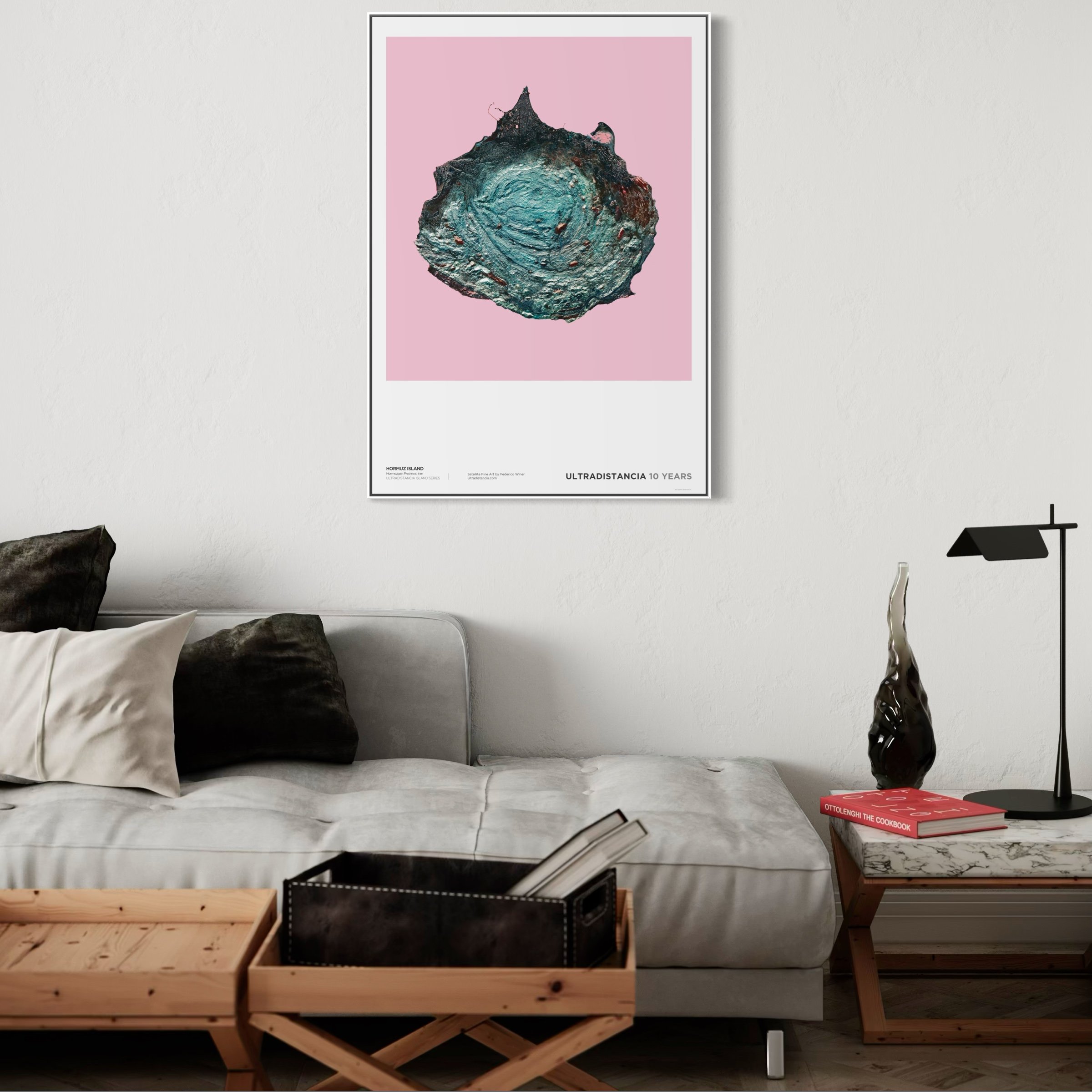 Interior of a modern living room with a white couch, decorative pillows, a wooden table, black wire baskets, and a framed artwork of a colorful, textured shell on a pink background hanging on the wall. Various books and objects are placed on surround