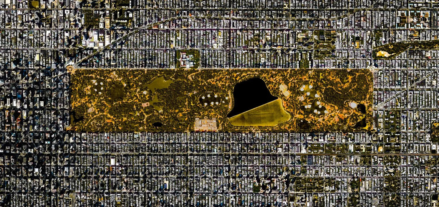 Aerial view of a large city park with a pond, surrounded by a grid of city streets and buildings.
