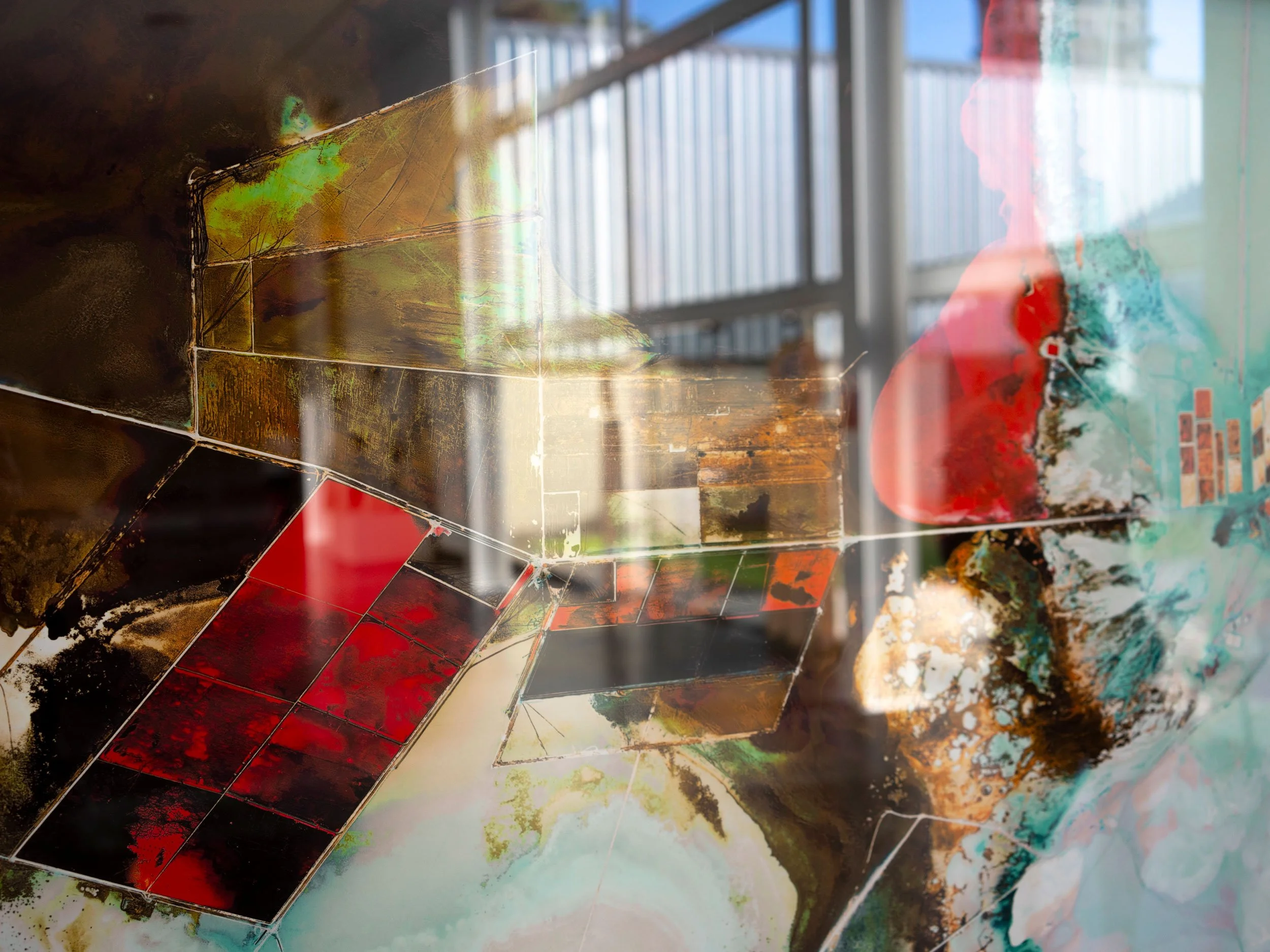 Close-up of a colorful abstract artwork with geometric shapes and layered textures, with a background suggesting a gallery or studio setting.
