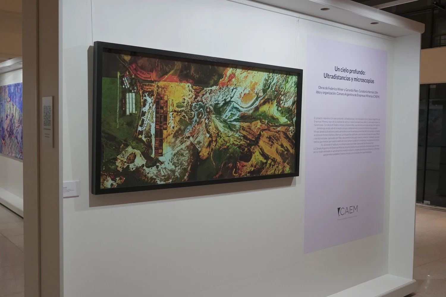 Colorful aerial map display at an art exhibit with a description panel titled 'Un cielo profundo: Ultradistancias y microscopías'