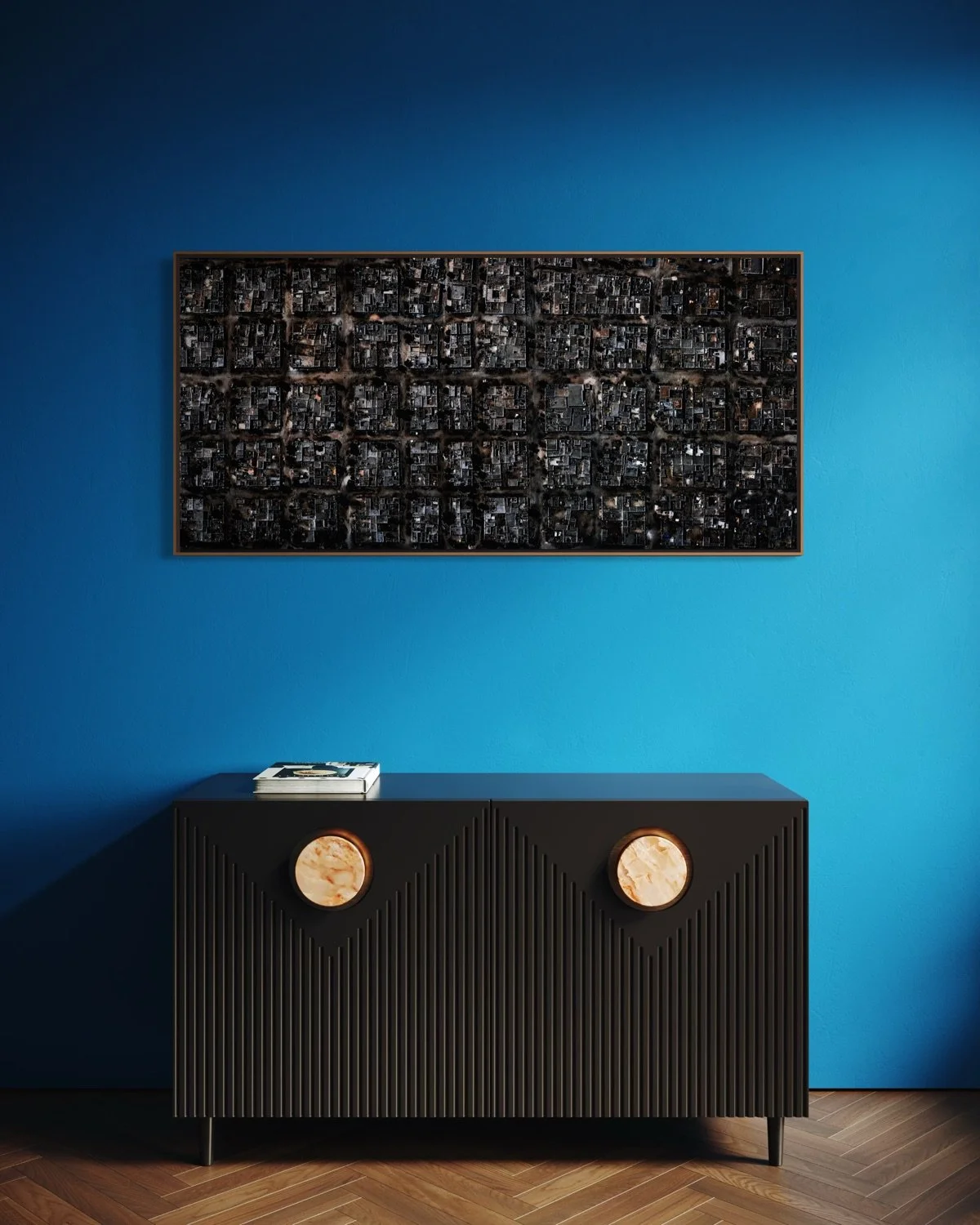 Modern black sideboard with textured vertical lines and two circular decorative pieces on a blue wall. A framed aerial city map hangs above and magazines sit on top of the sideboard. The room has a herringbone wooden floor.