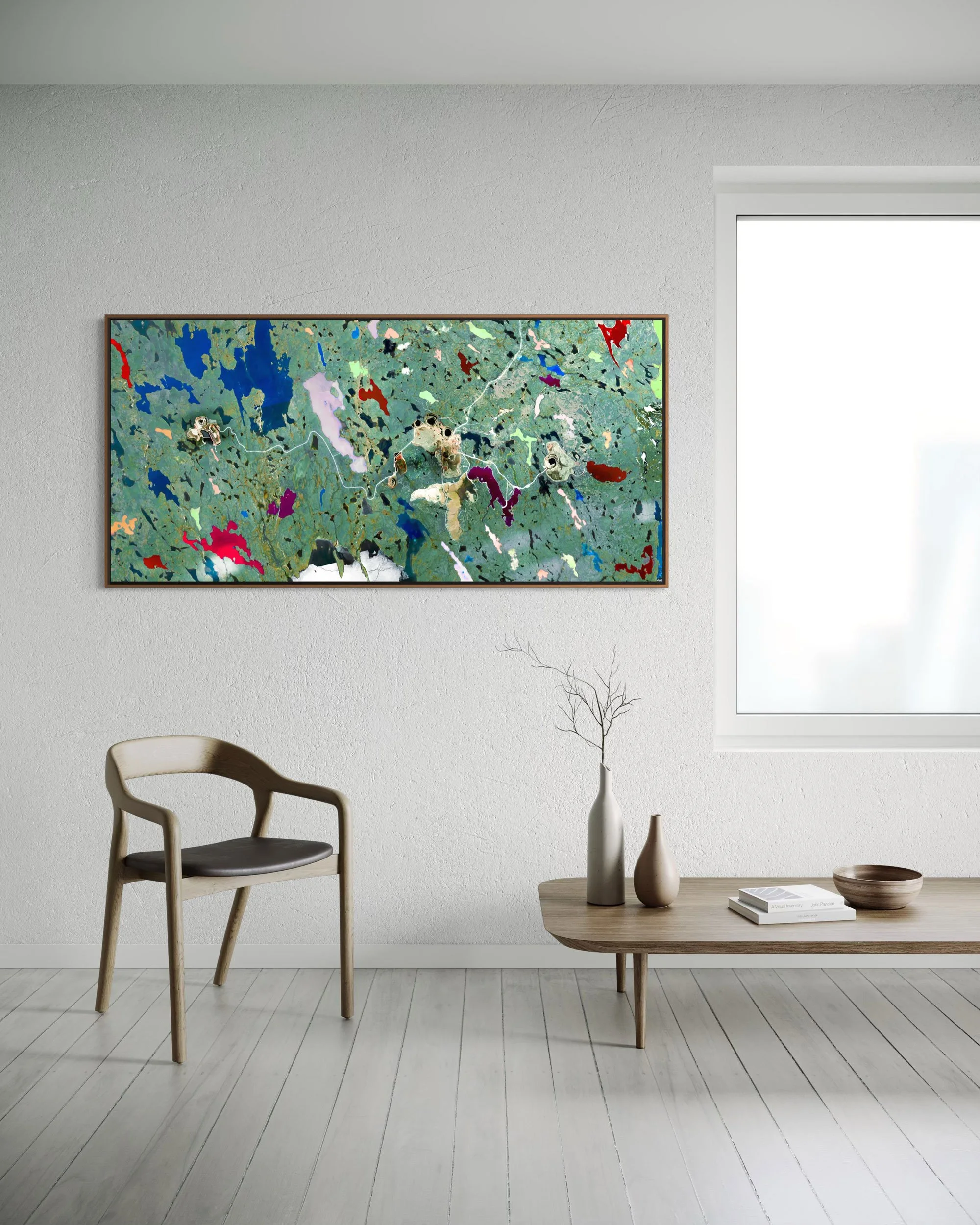Minimal interior showing a large framed panoramic Ekati Mine artwork on a pale wall, with a wooden chair, low table, and soft neutral decor.