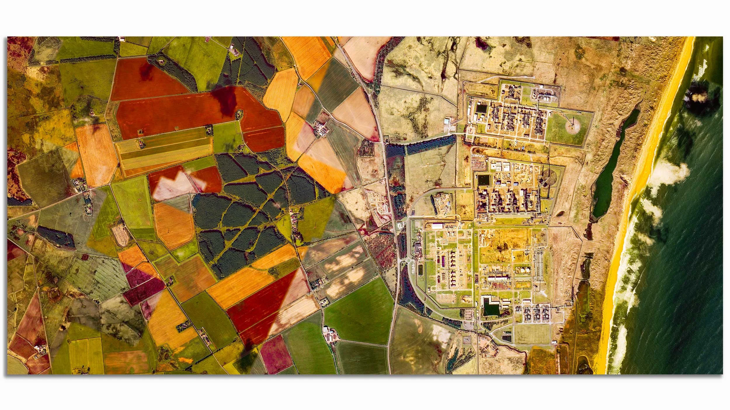Aerial view of colorful farmland, a coastal area with beach, and a town with buildings and roads.