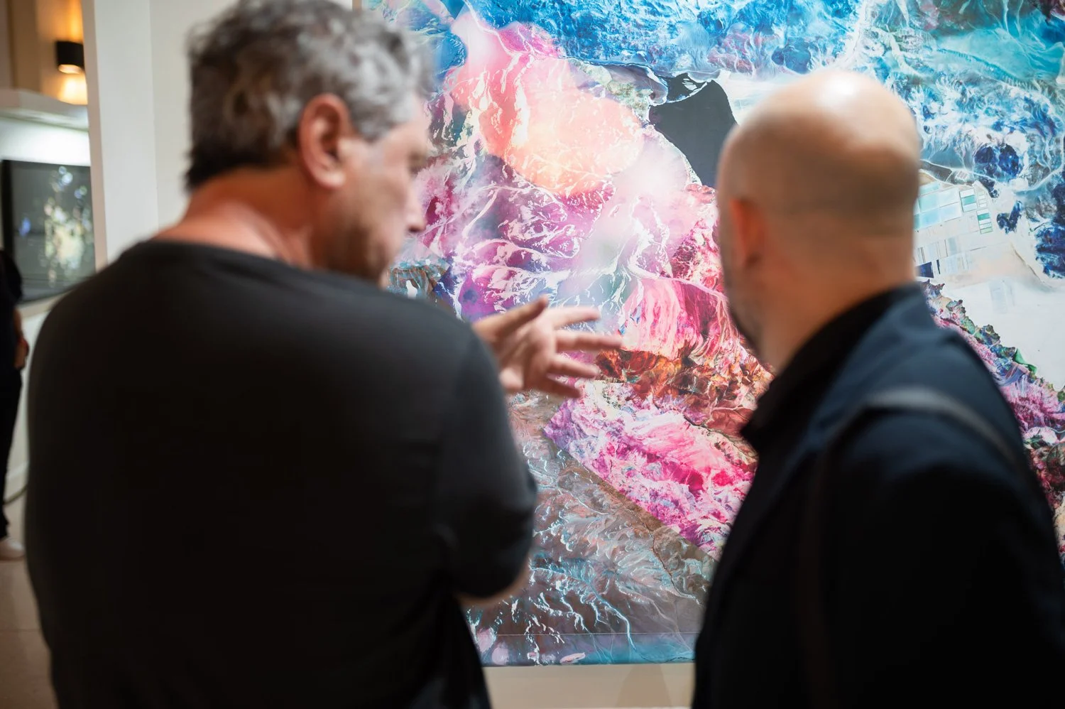 Two men in conversation looking at colorful abstract artwork in a gallery.