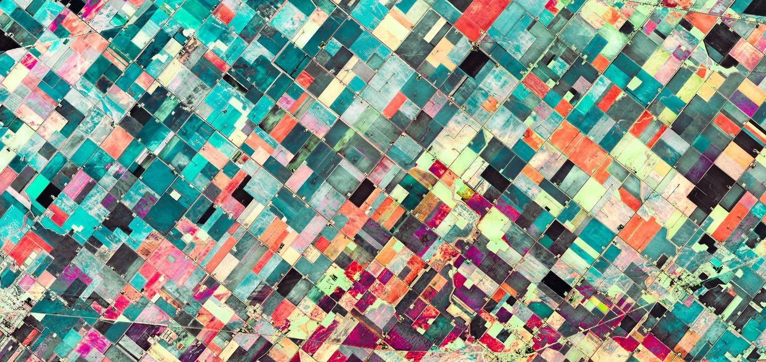 Aerial view of colorful agricultural fields divided by roads and irrigation canals.