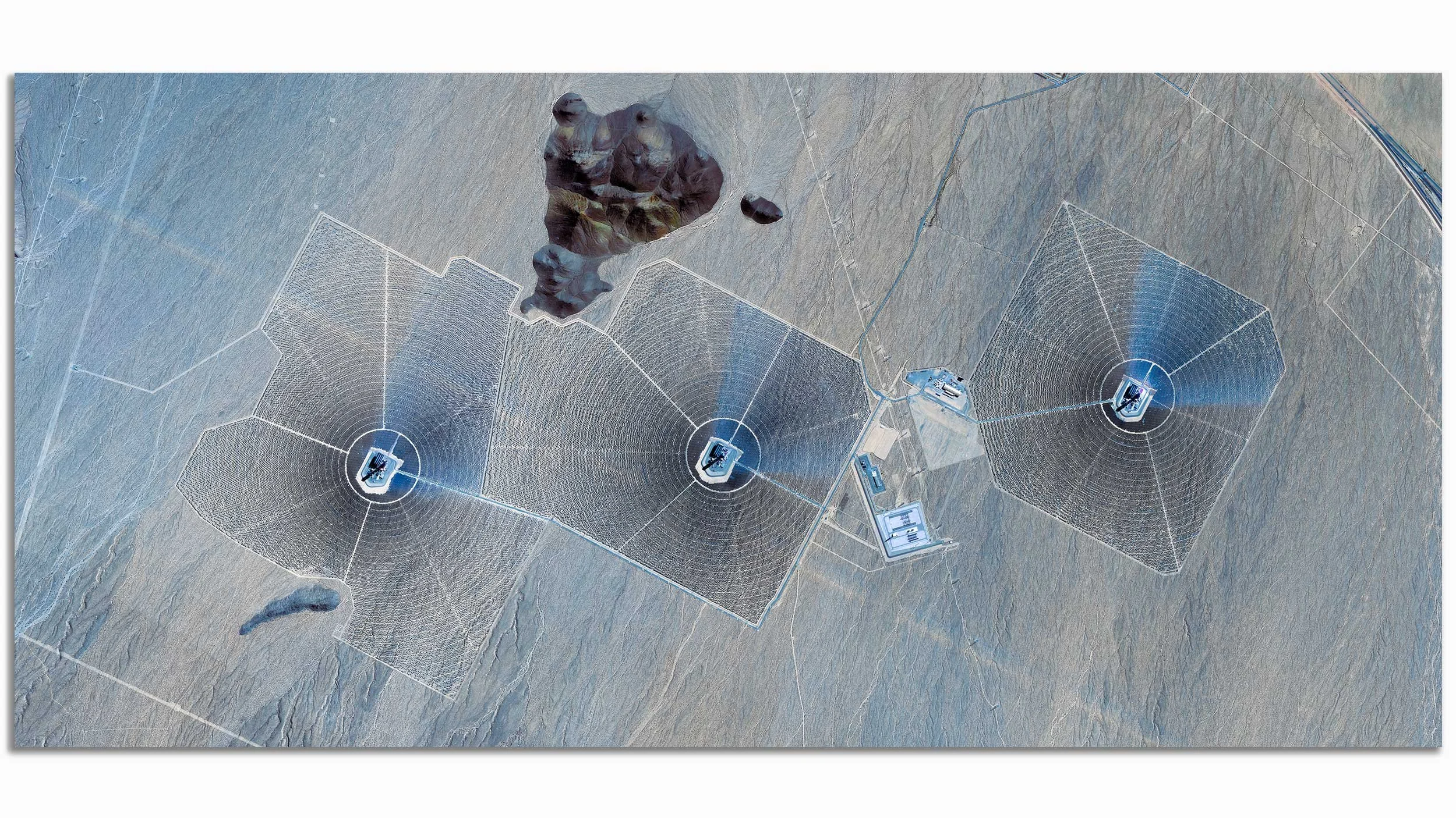 Aerial view of a solar farm with multiple large solar panel arrays and a satellite dish array in a desert landscape.