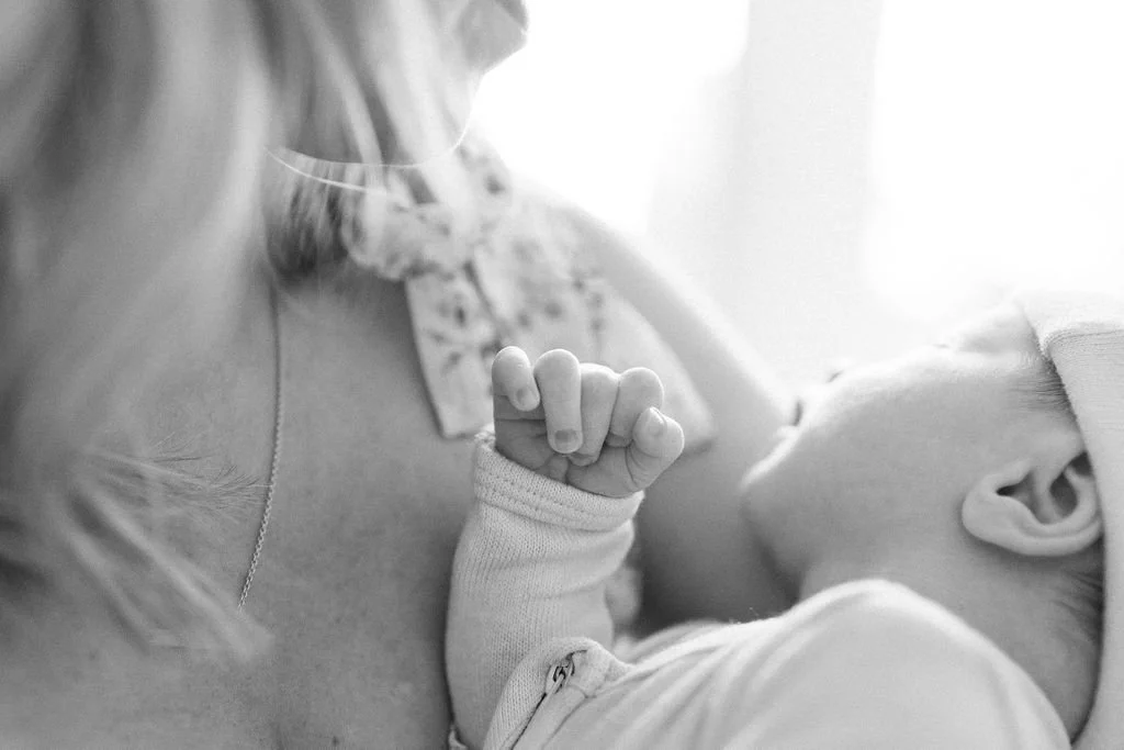 Black and white photograph focused on newborn baby's curling fingers while being held in mother's arms