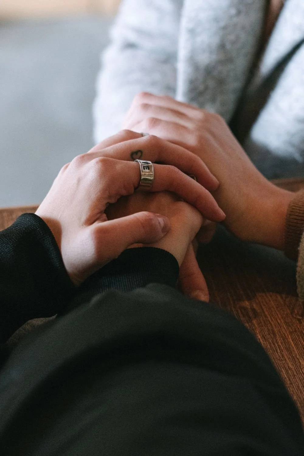 Two people holding hands, one wearing a ring that says 'LOVE'.