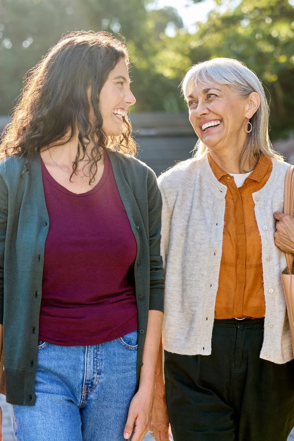 Two women smiling and walking outdoors on a sunny day, engaging in a conversation.
