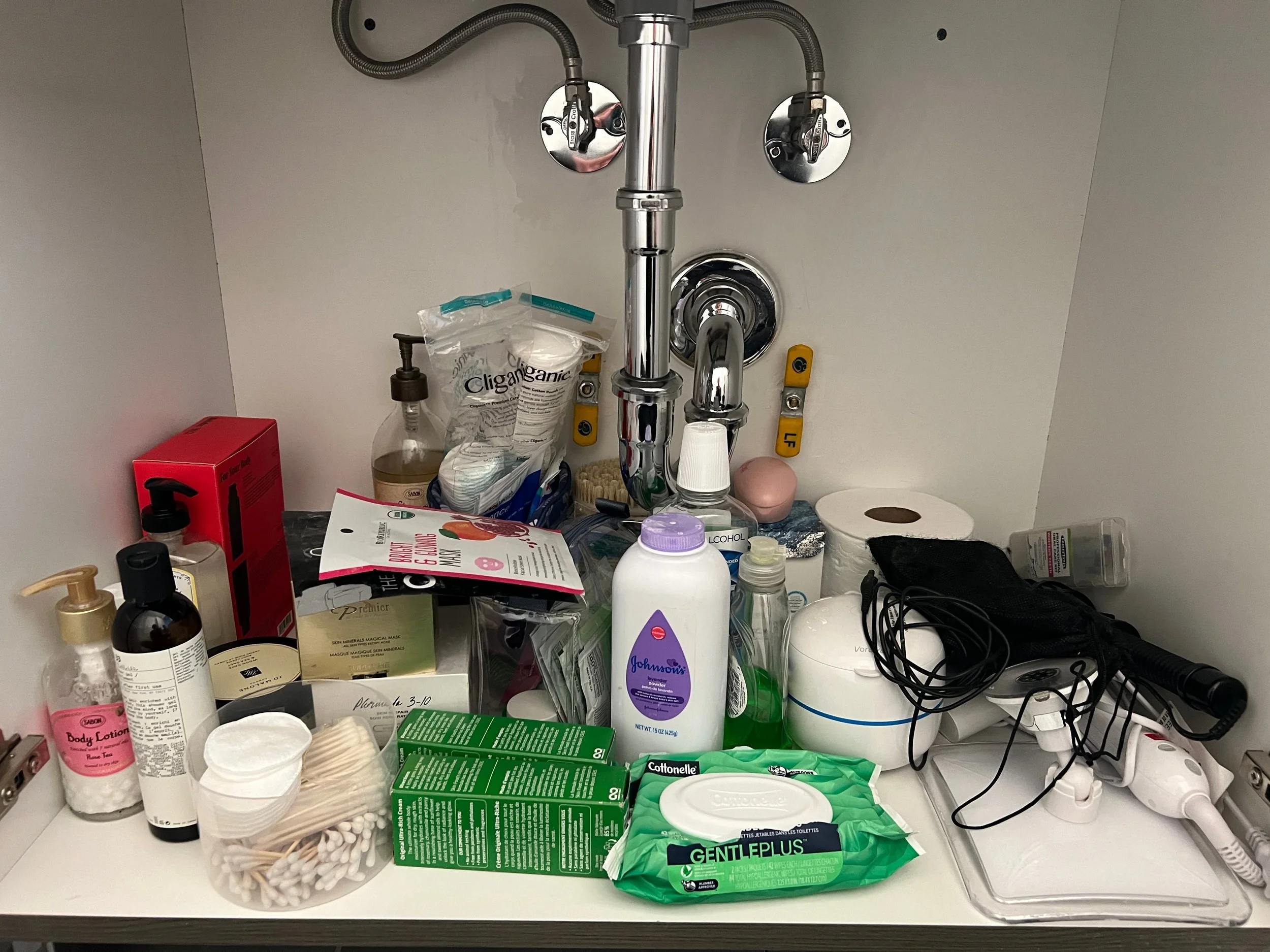 Under sink area cluttered with wires and cleaning and beauty products