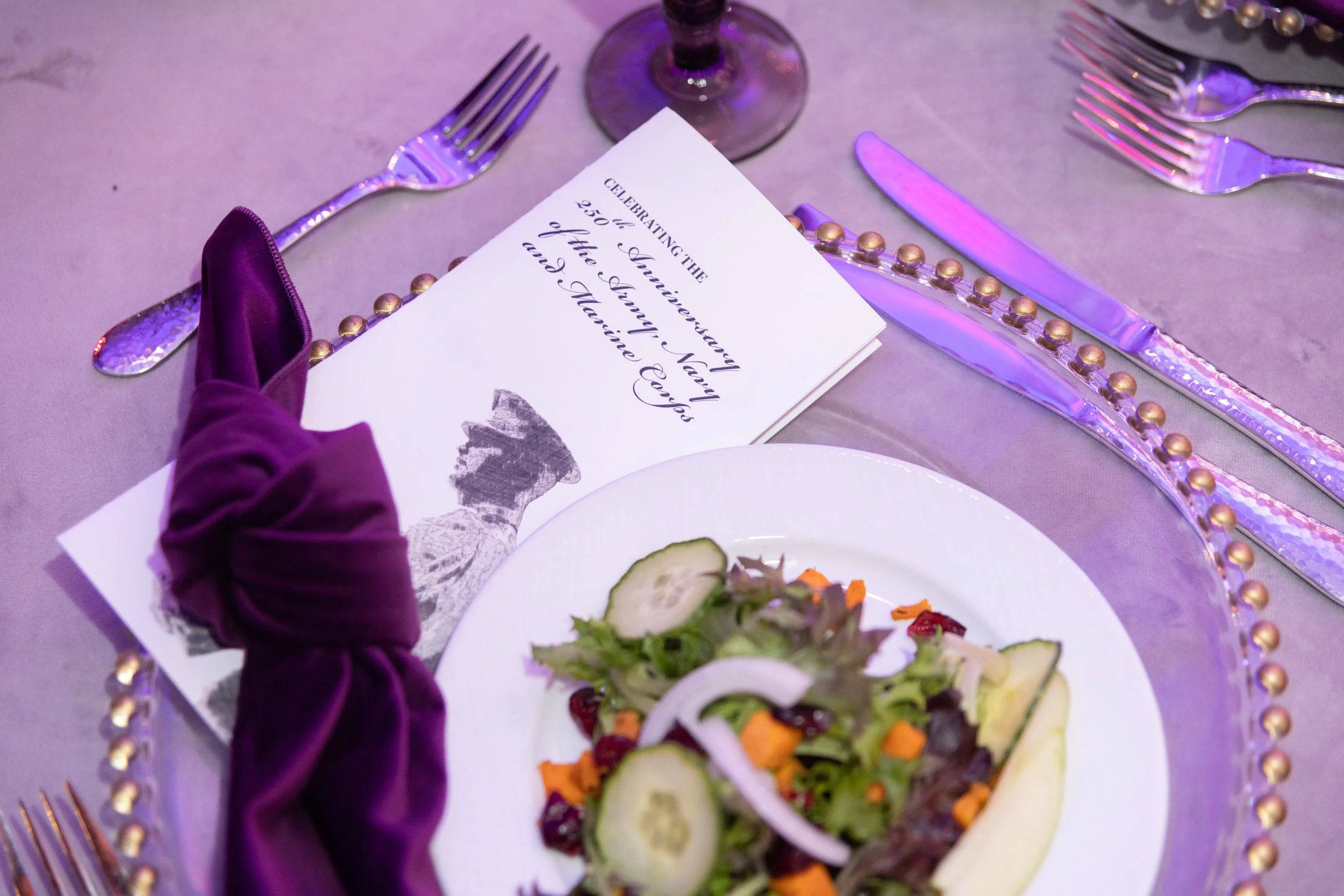 Table setting with the program for the event stating "Celebrating the 250th Anniversary of the Army, Navy and Marine Corps