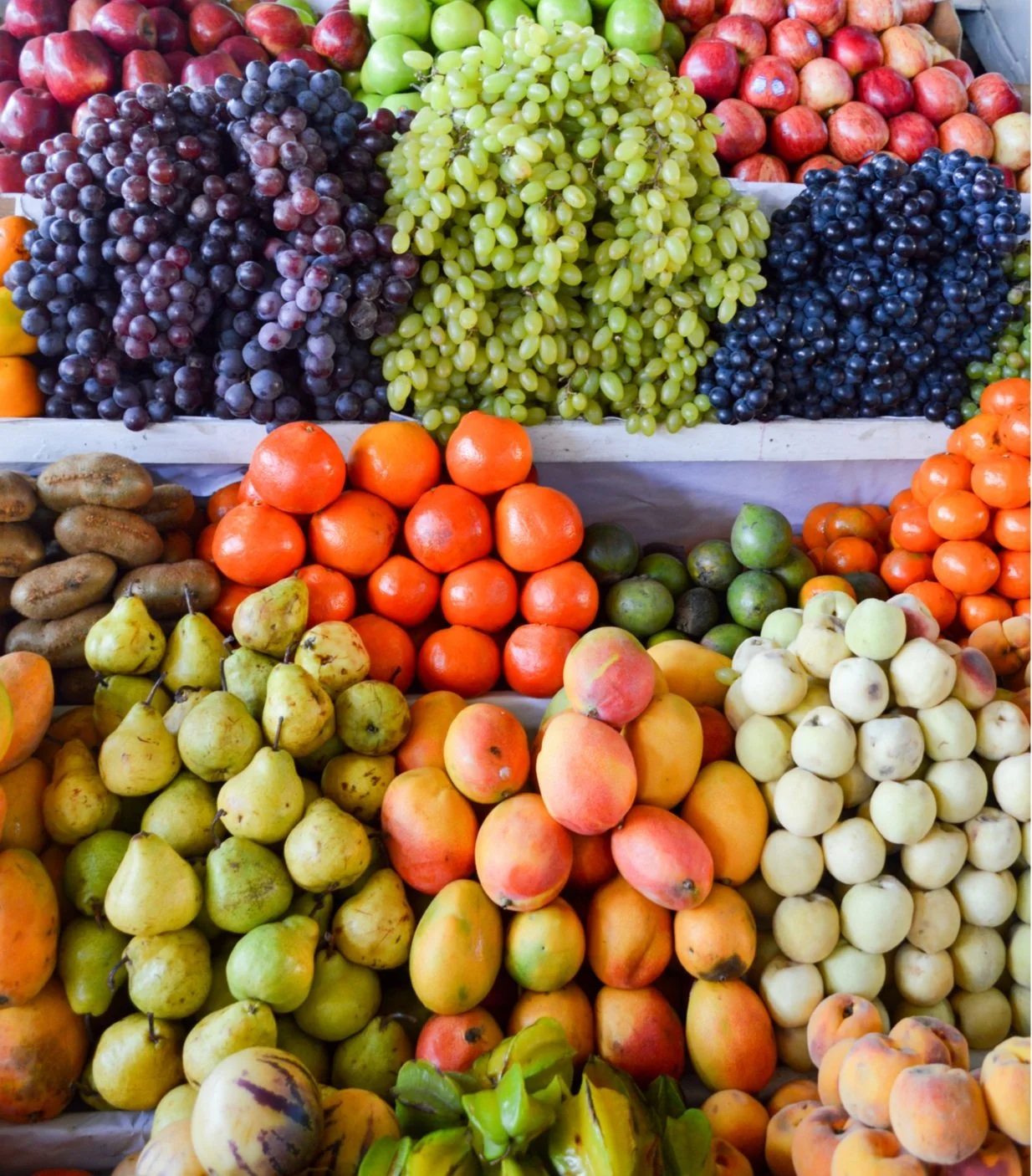 Display of fresh grapes, apples, pears, peaches, and other assorted fruits at an outdoor market.