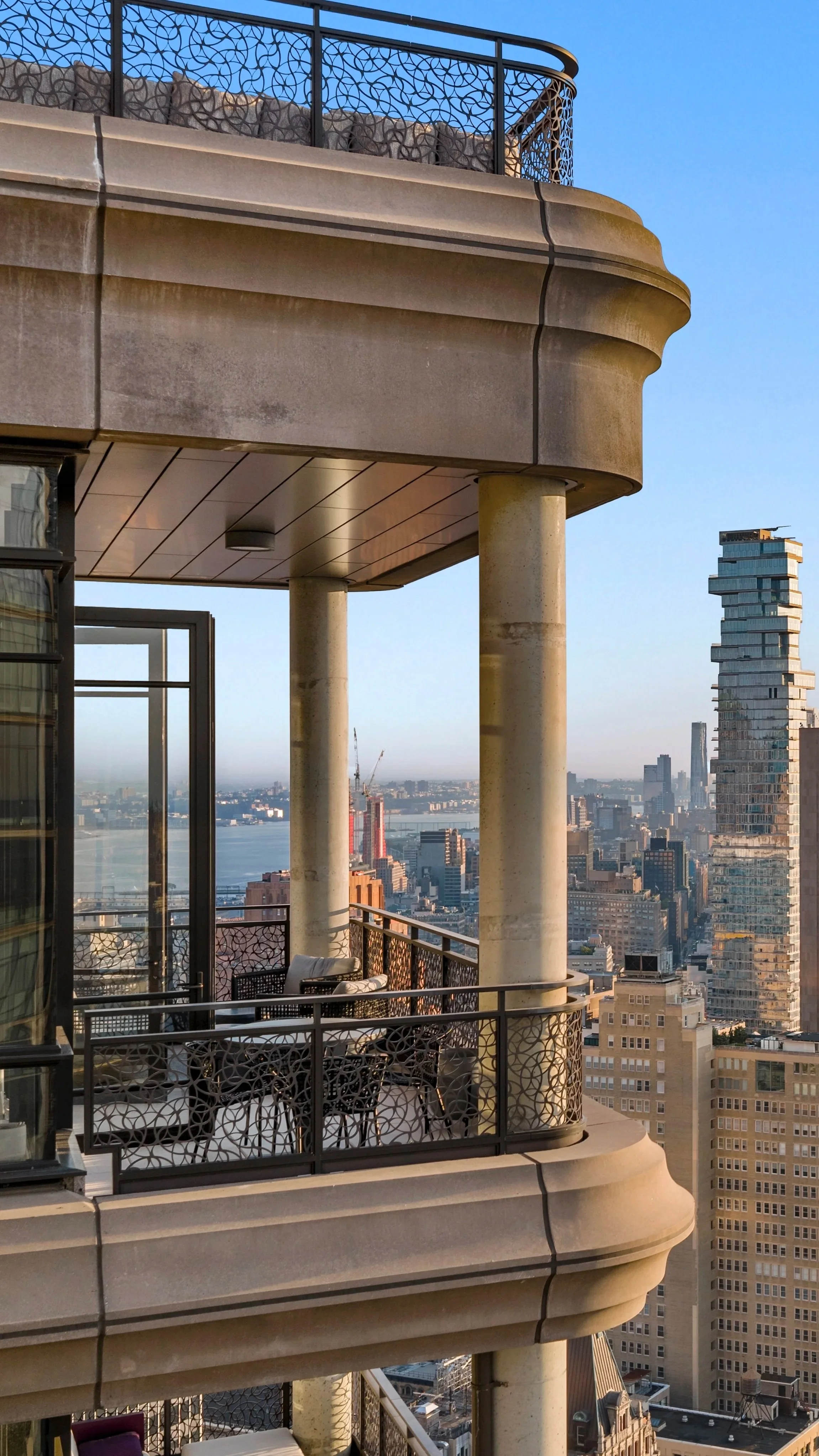 View from a high-rise balcony with ornate railing, showing a city skyline with tall buildings and a river in the background.