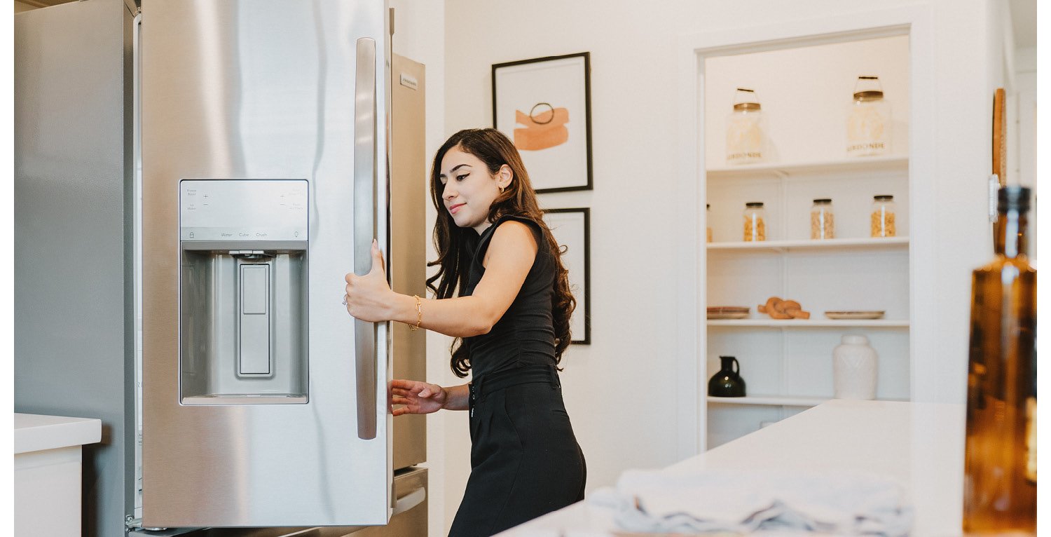 Young lady opening refrigerator door to peek inside.