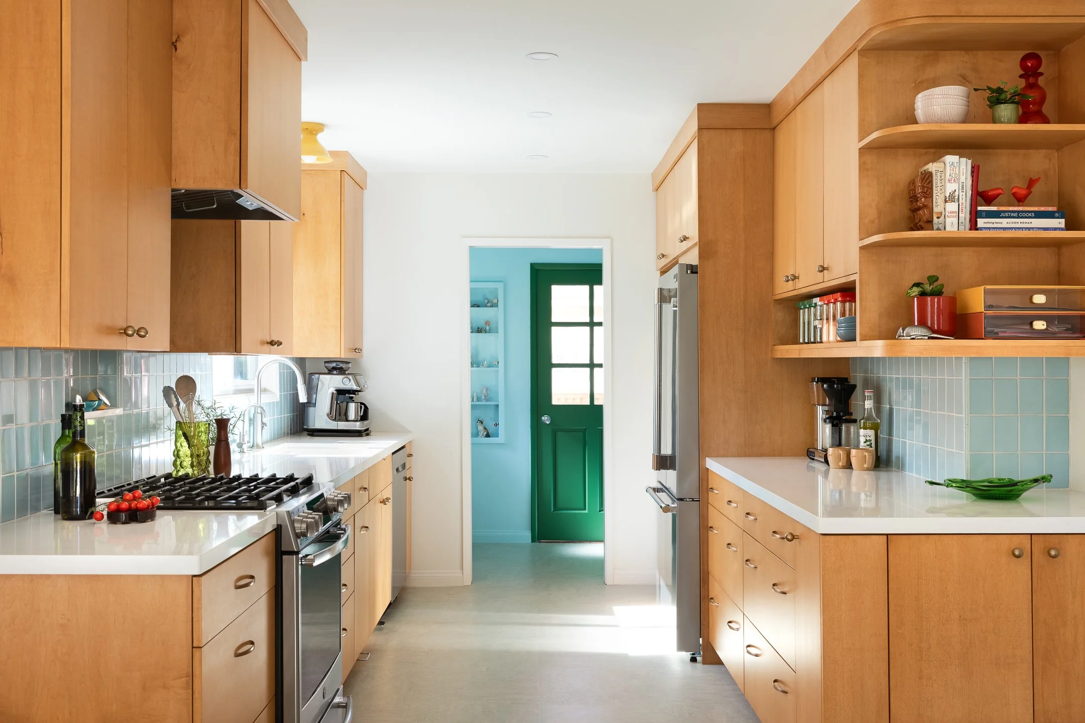 Bright kitchen with wood cabinets, white countertops, and a turquoise door leading outside.
