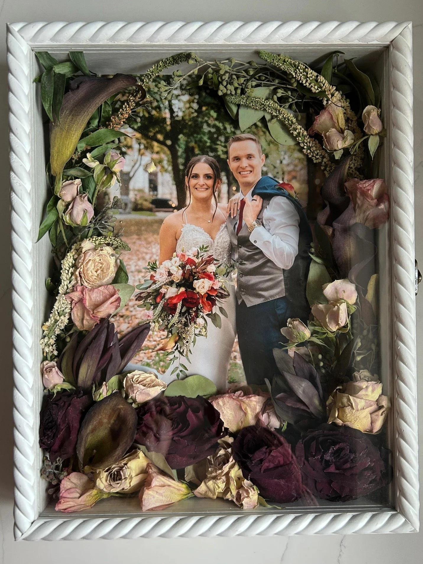 11x14 white braided shadow box with 8x10 photo of bride and groom featuring lilies, lisianthus, and spray roses (horseshoe floral design)