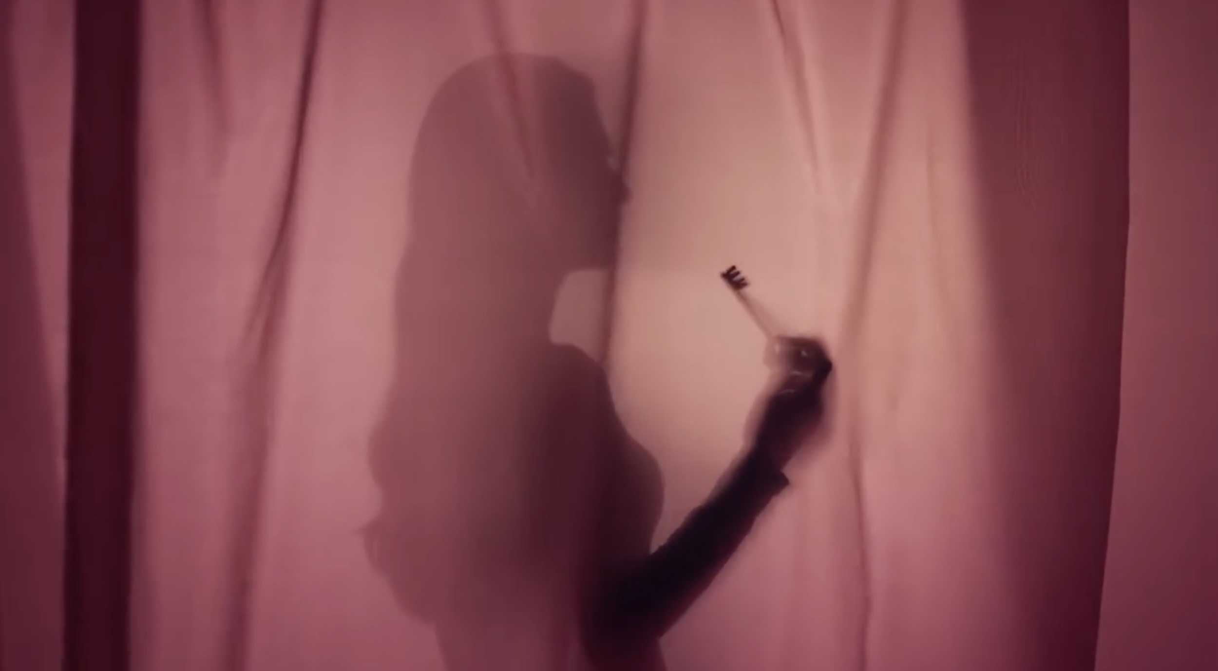 A person writing on a pink curtain with a black marker, creating a silhouette profile of a face.