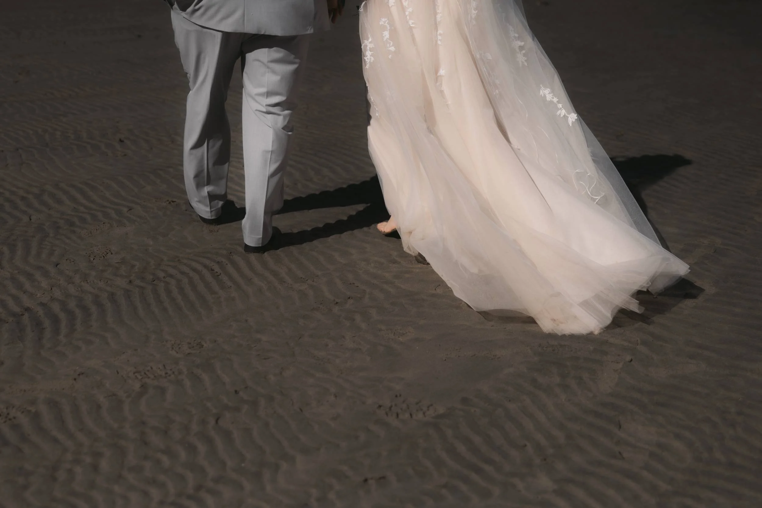 Wedding dress moving across the rippled sand during beach portraits in Parksville