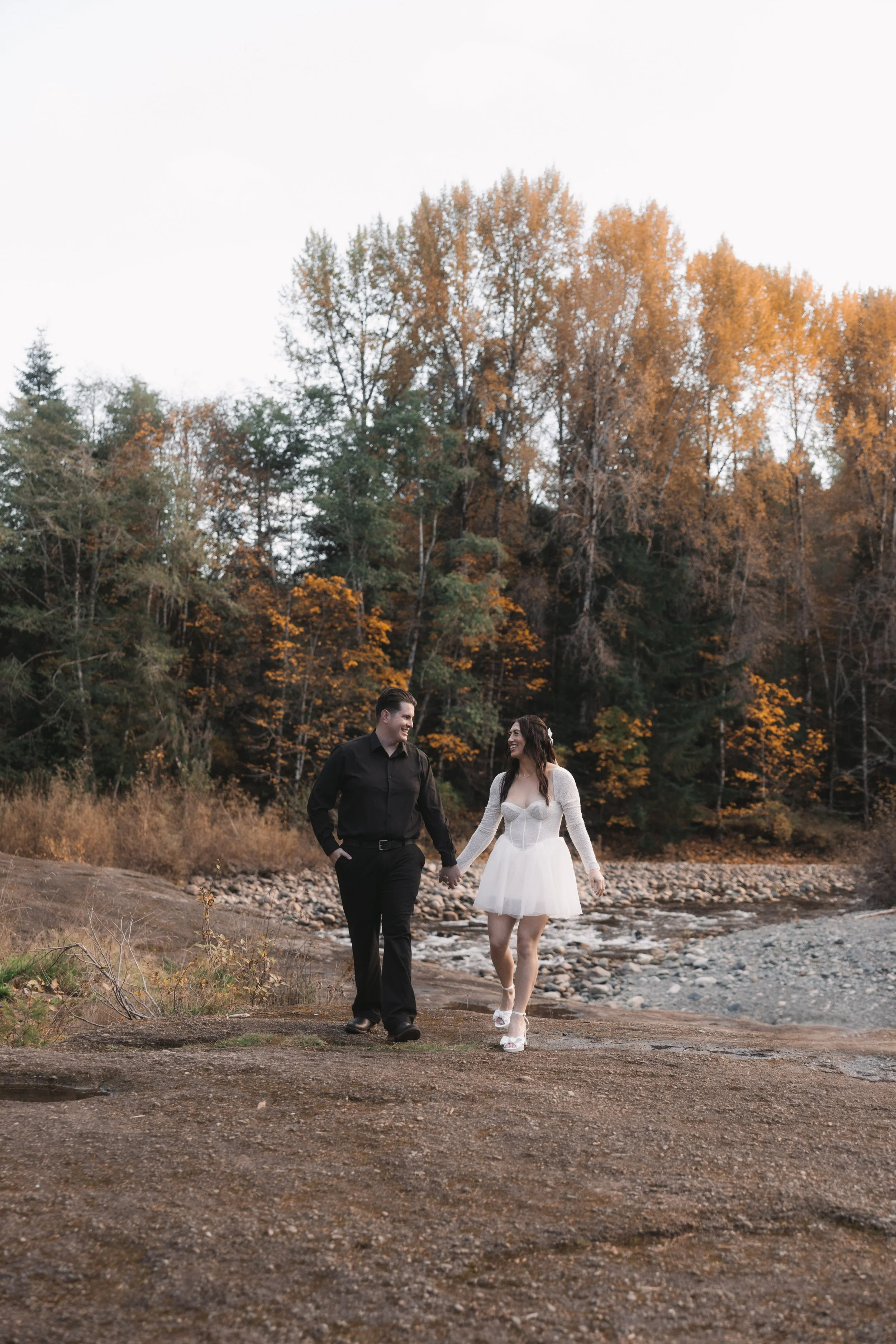 Gina and Jacob walking beside the Englishman River at Top Bridge Park during a Parksville engagement photography session