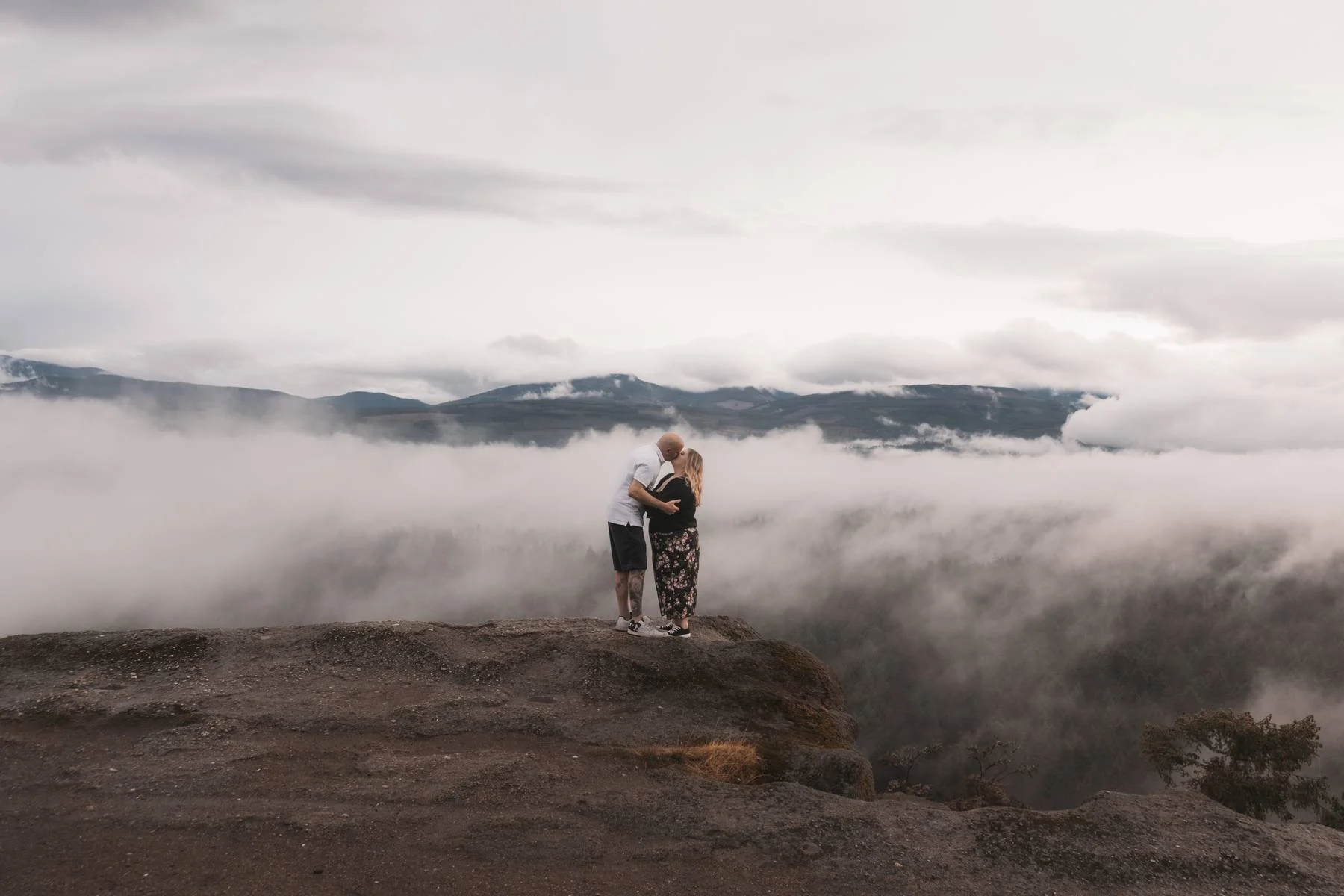 Couple kissing at Little Mountain with clouds drifting across the mountains during their Parksville engagement session