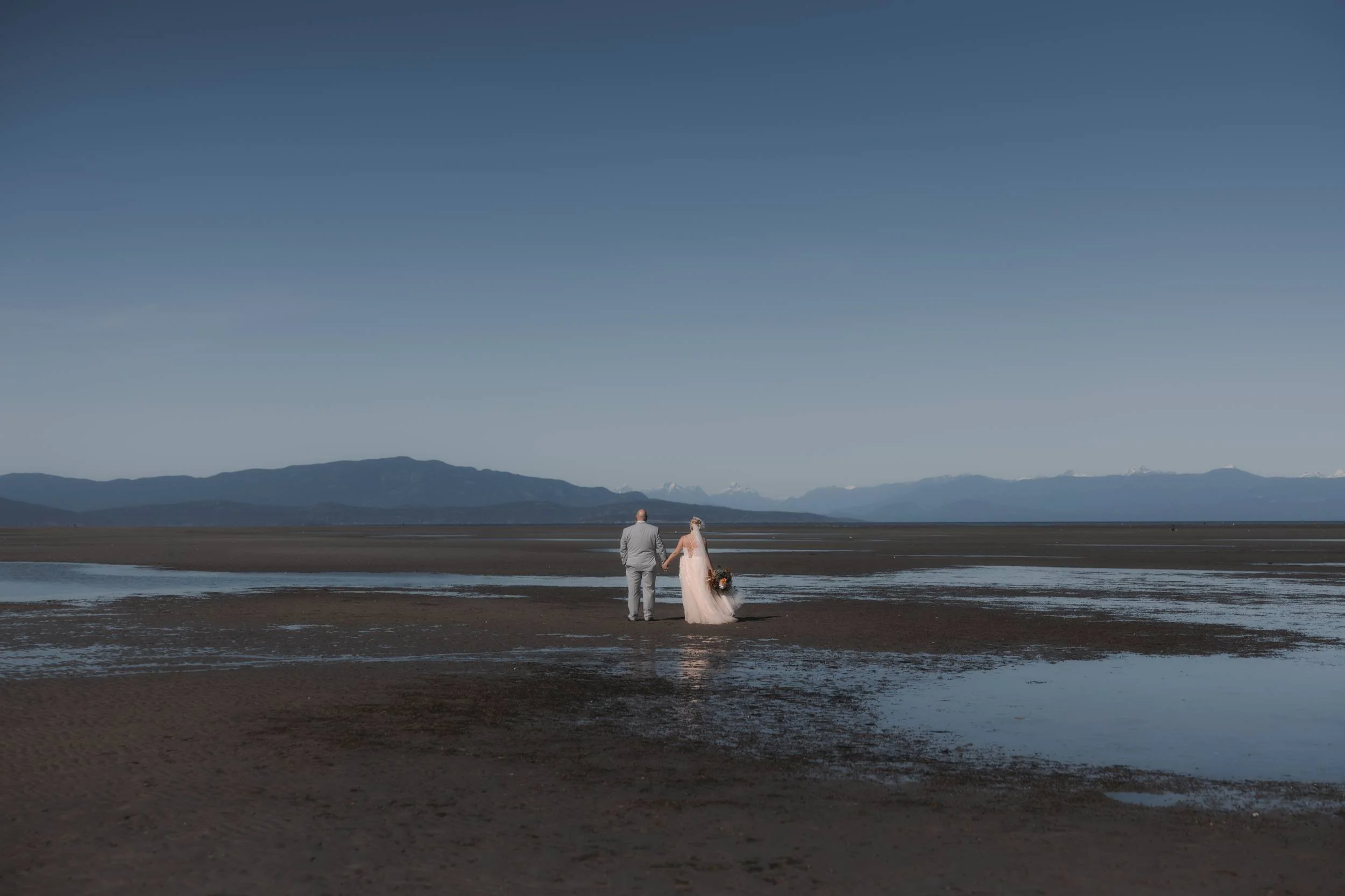 Newlyweds walking across the beach at low tide near Tigh-Na-Mara in Parksville, BC