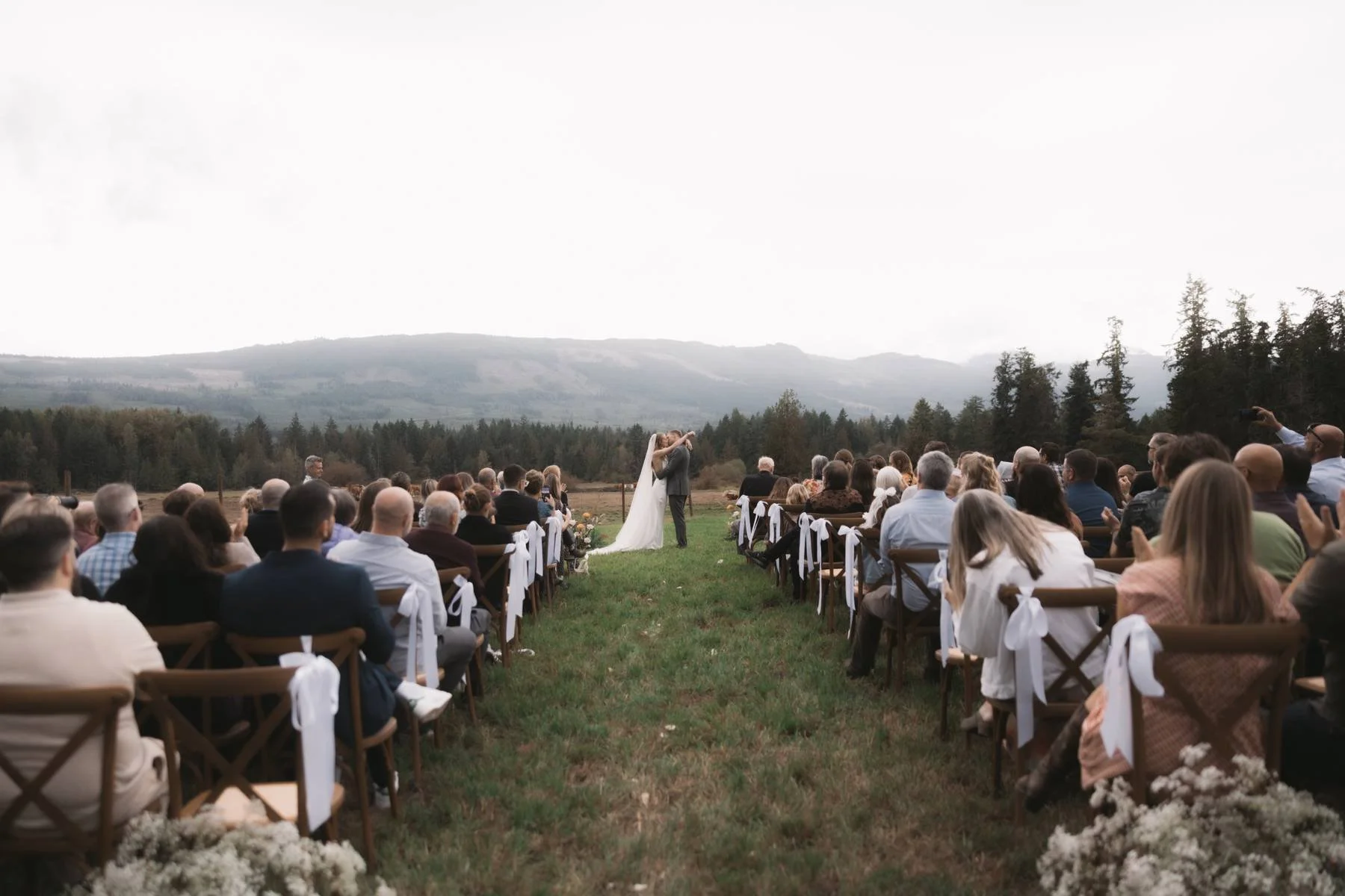 Outdoor wedding ceremony with mountain views on Vancouver Island, bride and groom kissing at altar surrounded by guests