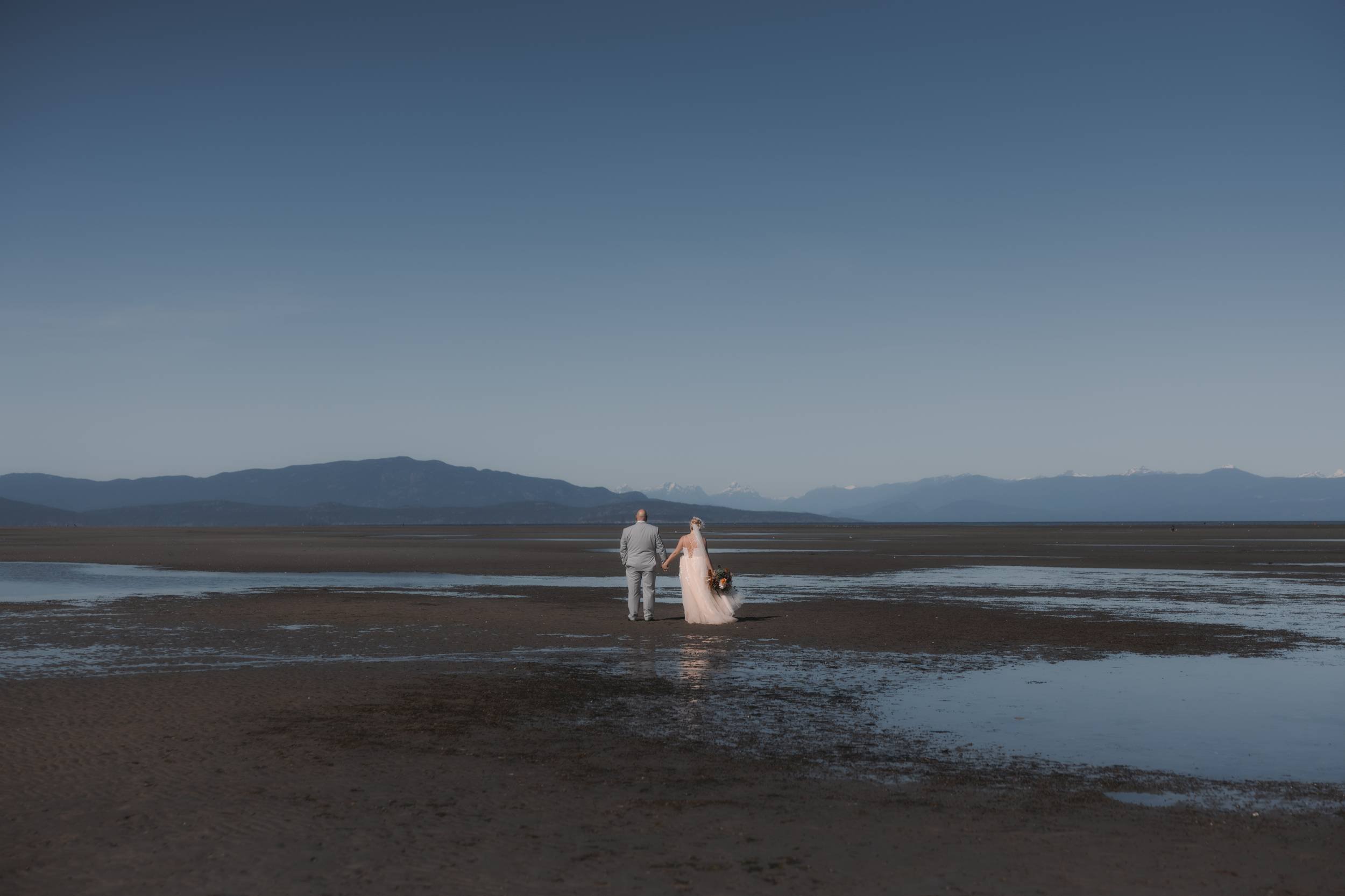 Taliah and John walking together across the low-tide beach near Rathtrevor in Parksville