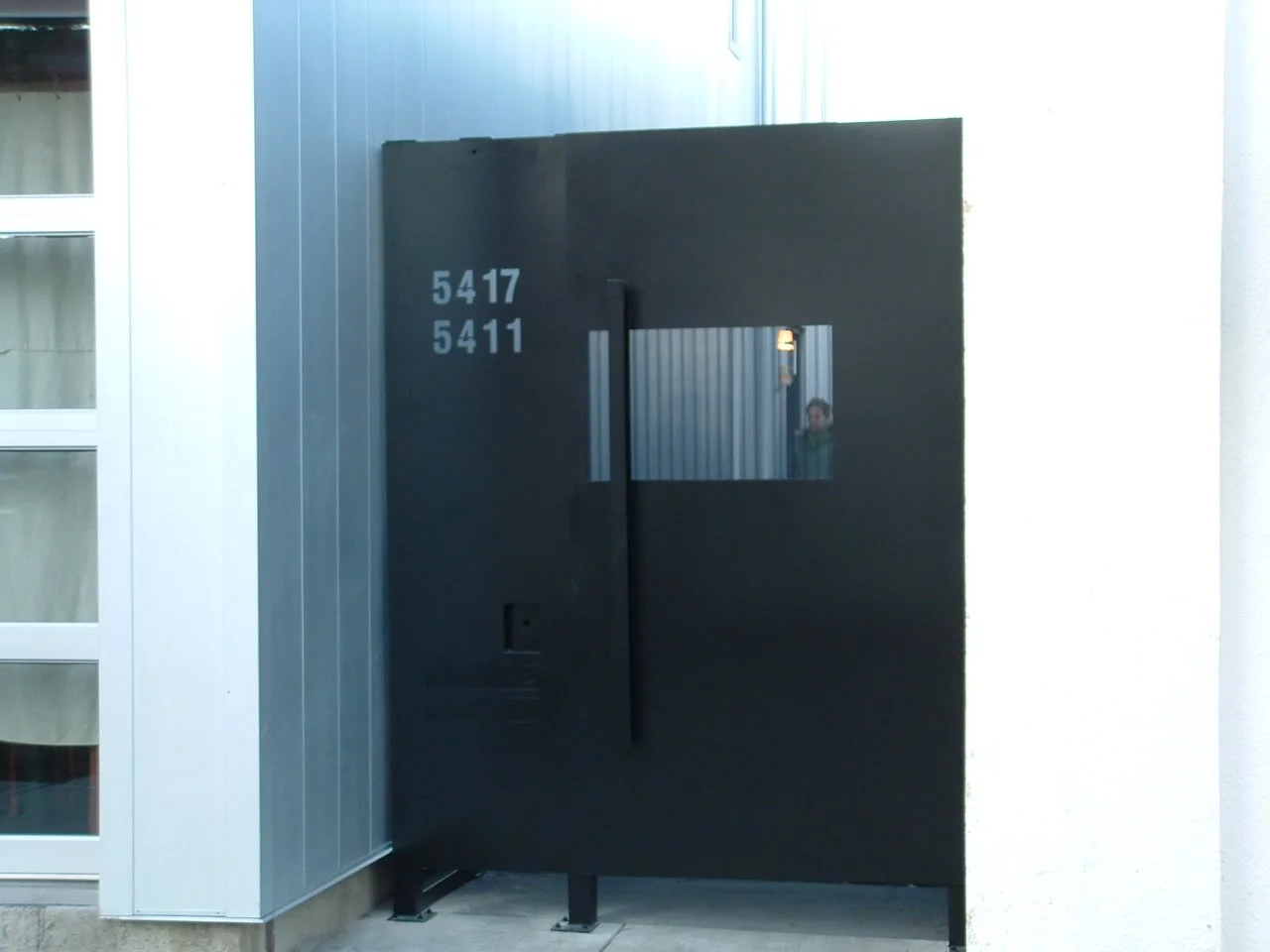 Black modern building with numbers 5417 and 5411 on the wall, reflecting a person in a small window.