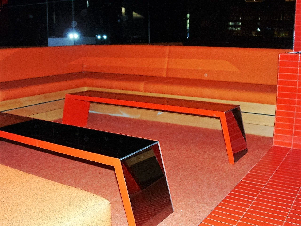 Interior of a room with modern red and black furniture, including two slanted tables, beige seating, and red tiled walls and flooring.