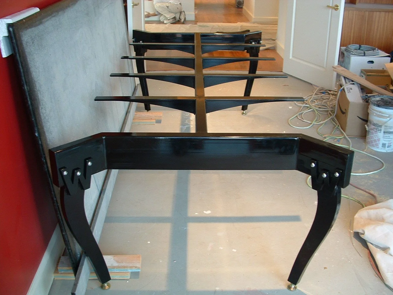 The image shows a black table frame being assembled or painted, with other furniture and household items around, inside a house under renovation or reorganization.