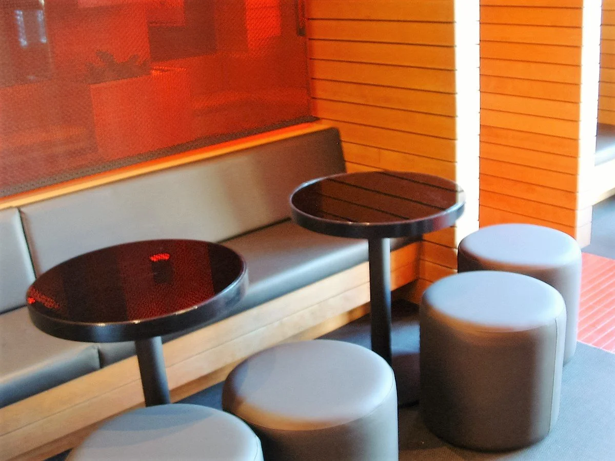 Indoor seating area with a bench, two small round tables, and three stools in front of a wooden wall.