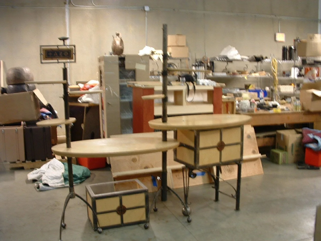 A warehouse with various items, including tables, boxes, shelves, and miscellaneous objects.