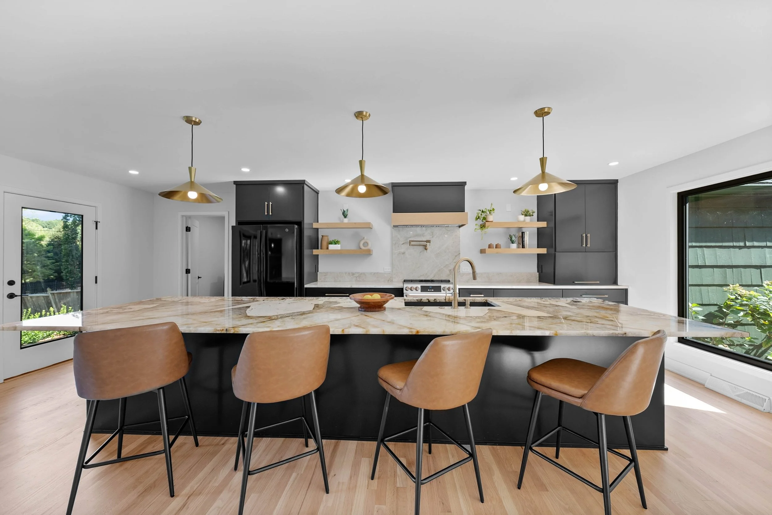 Bold &amp; built for gathering. ✨

This kitchen was designed to make a statement. From the massive waterfall island and rich black cabinetry to the warm brass accents and natural wood shelving, every detail works together to create a space that&rsquo