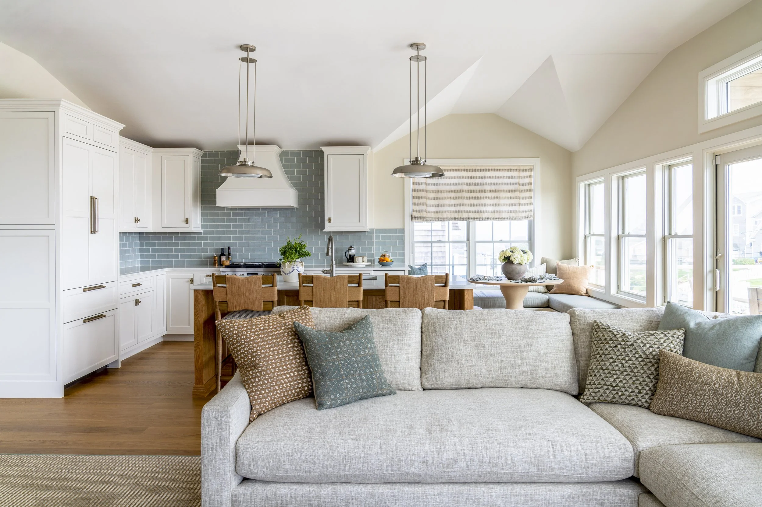 Open kitchen and family room with vaulted ceilings and layered coastal furnishings in a Narragansett, Rhode Island beach house by Blakely Interior Design.