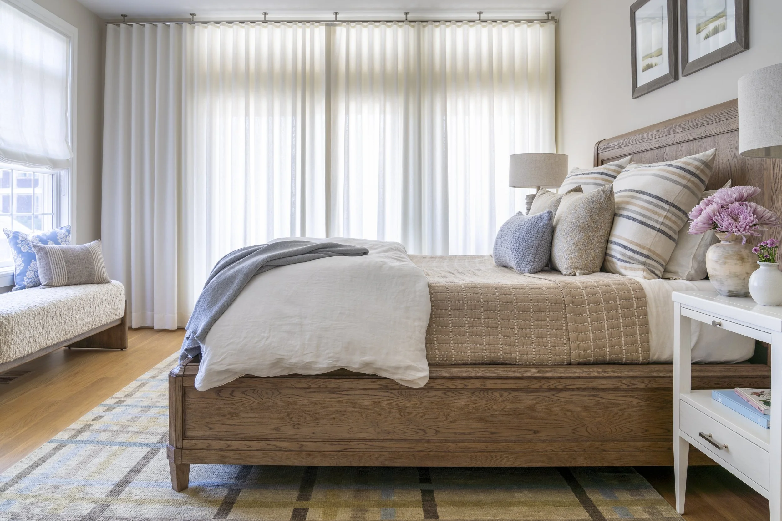 Light-filled coastal bedroom with upholstered chaise, layered textiles and natural wood details in Narragansett, RI.