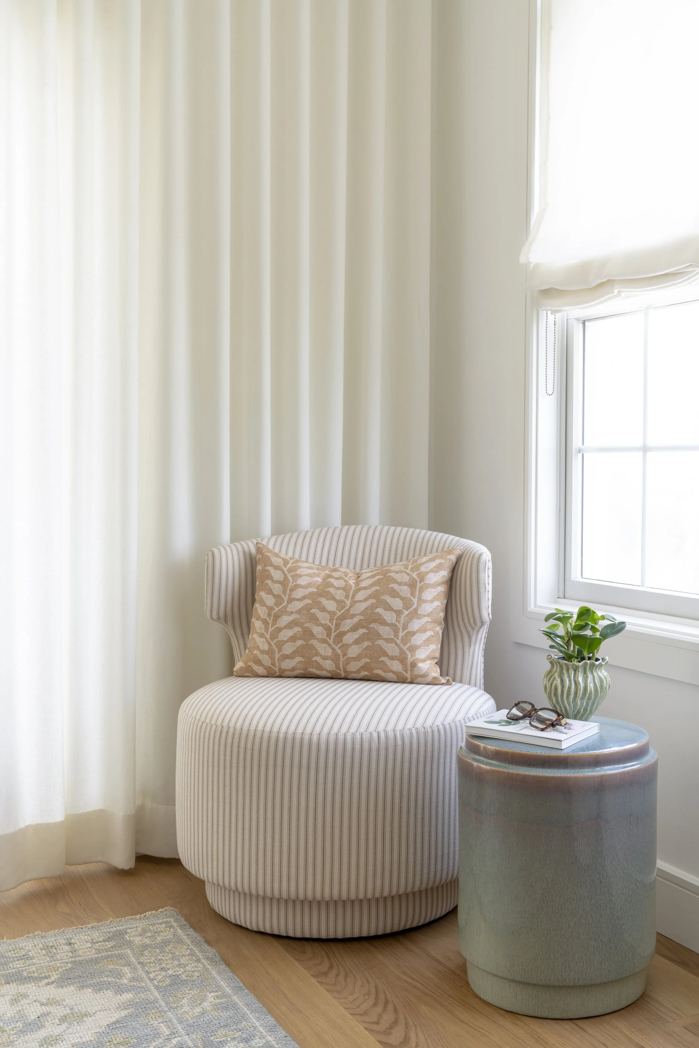 Quiet bedroom sitting nook with curved upholstered chair, ceramic side table and soft natural light in a Narragansett beach house.