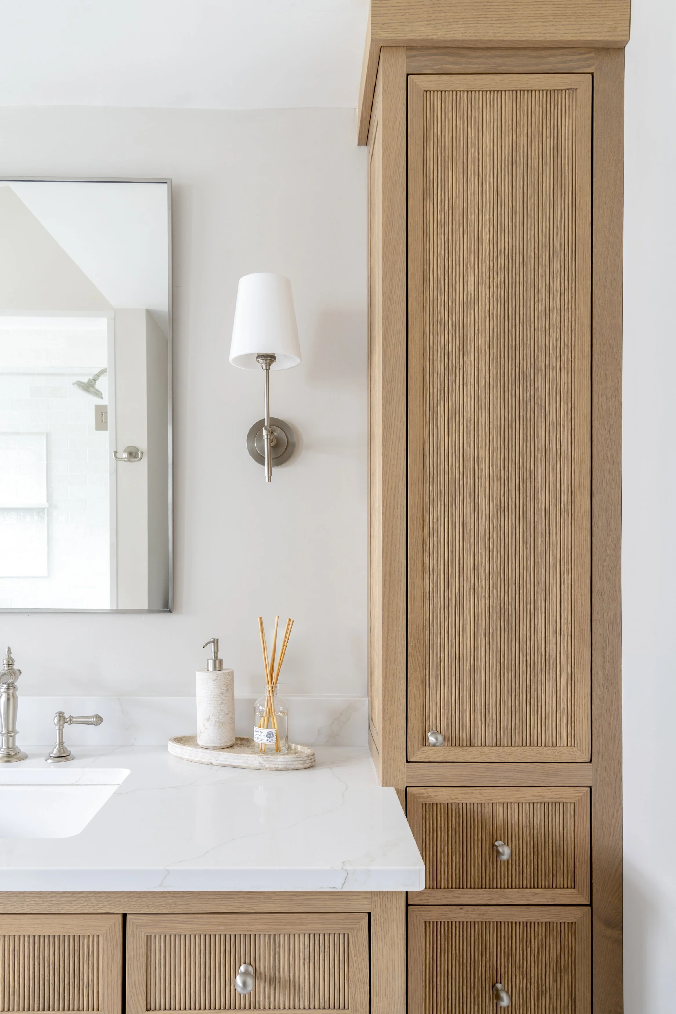 Primary bathroom detail with reeded wood cabinetry, marble countertop and custom storage by Blakely Interior Design.