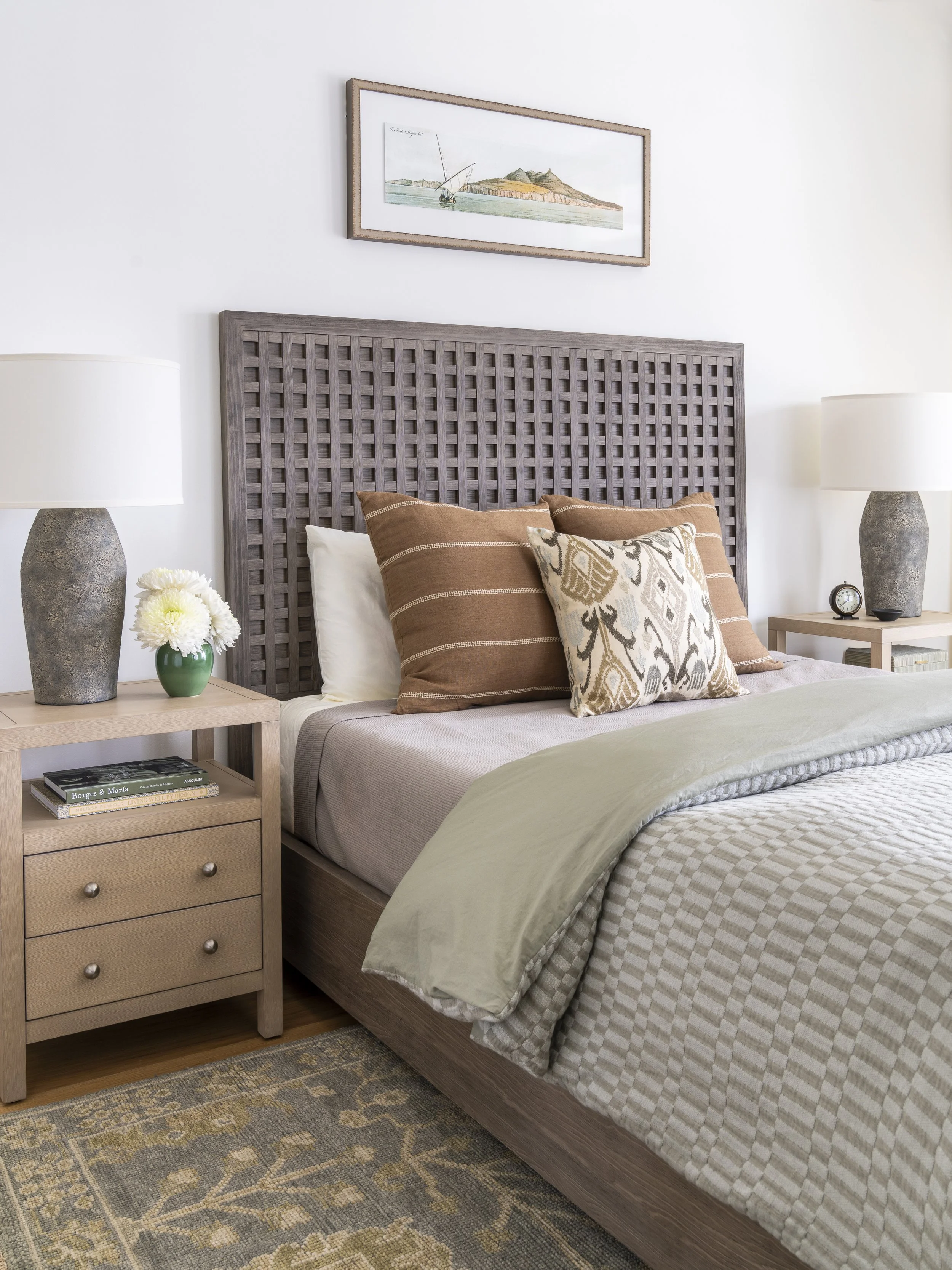 Warm neutral bedroom with woven headboard, layered bedding and natural wood furniture in a Narragansett beach house.