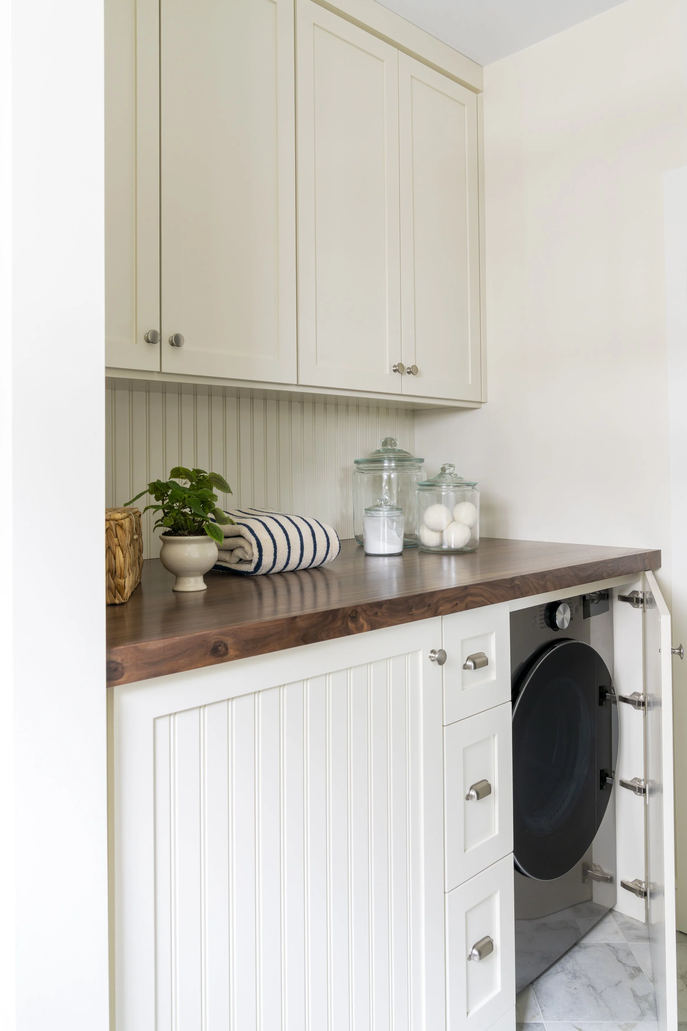 Integrated laundry cabinetry with white beadboard doors and warm wood countertop designed by Blakely Interior Design.