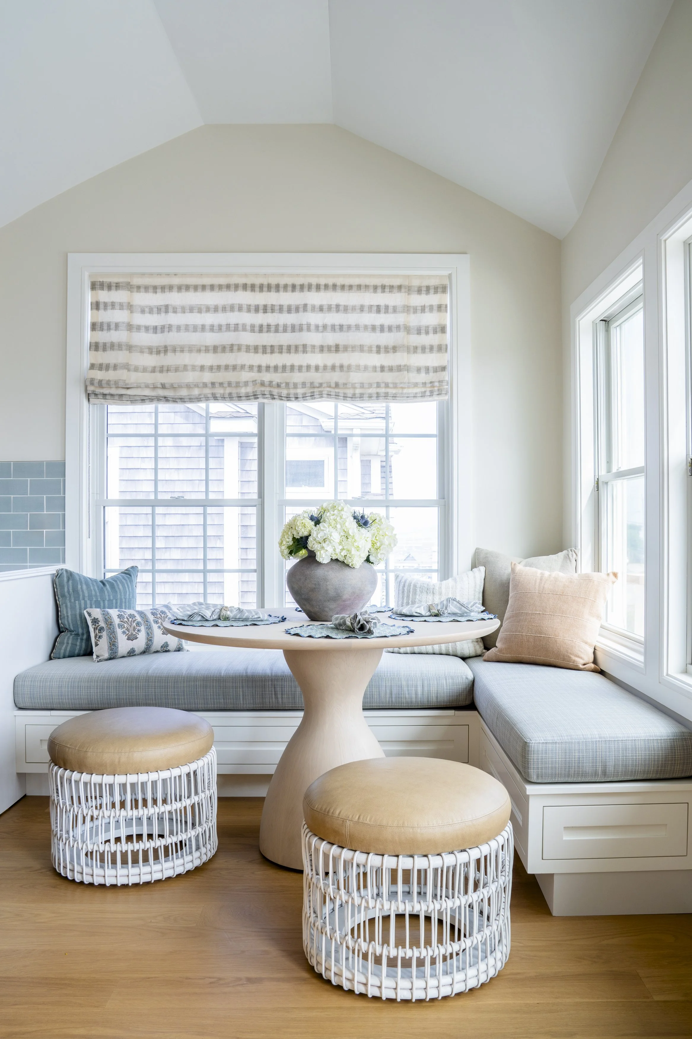 Built-in breakfast banquette with soft blue upholstery and woven stools in the Jerusalem Heights beach house in Narragansett, RI.