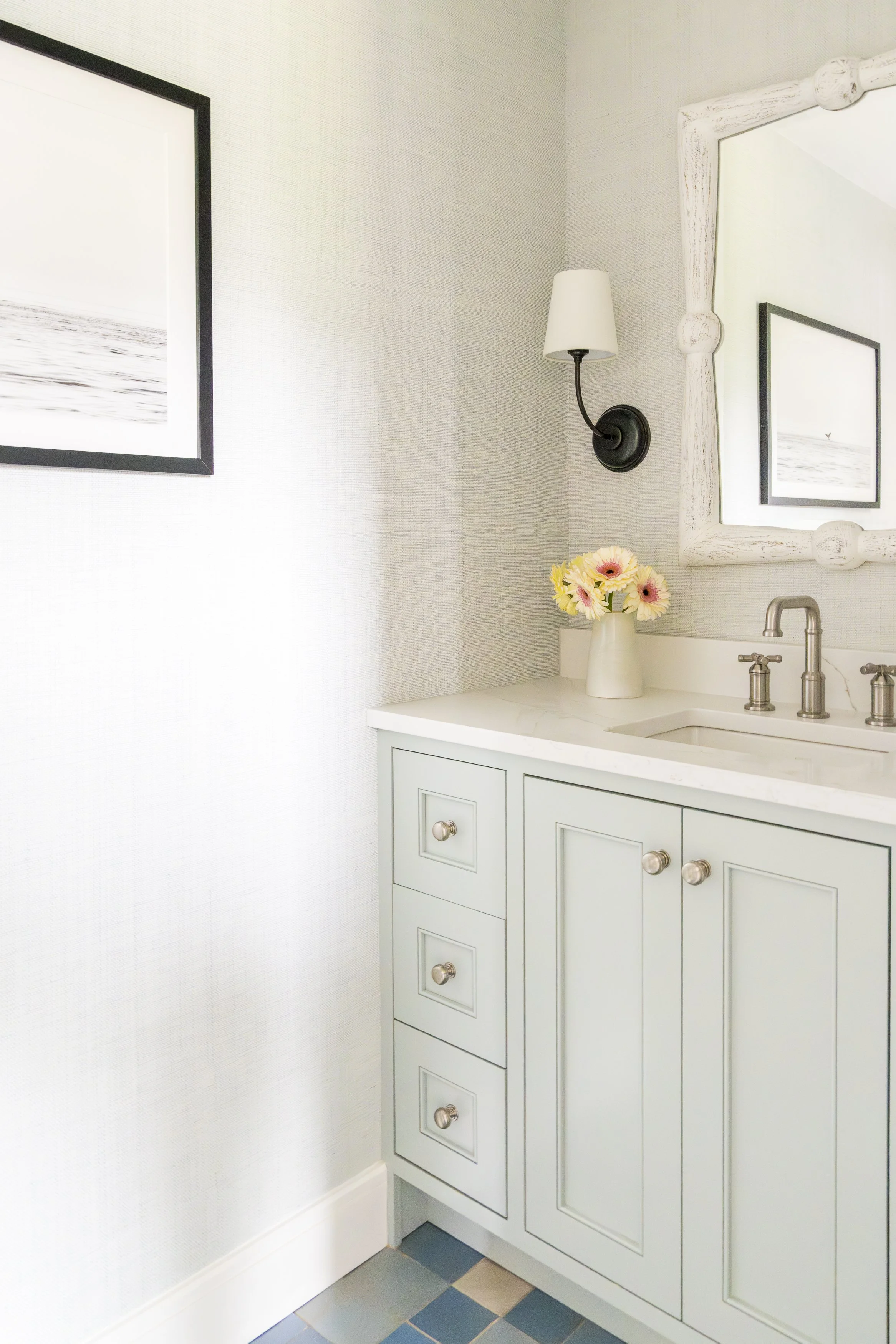 Pale green bathroom vanity with brass hardware and blue checkerboard tile floor in a renovated Narragansett beach house.