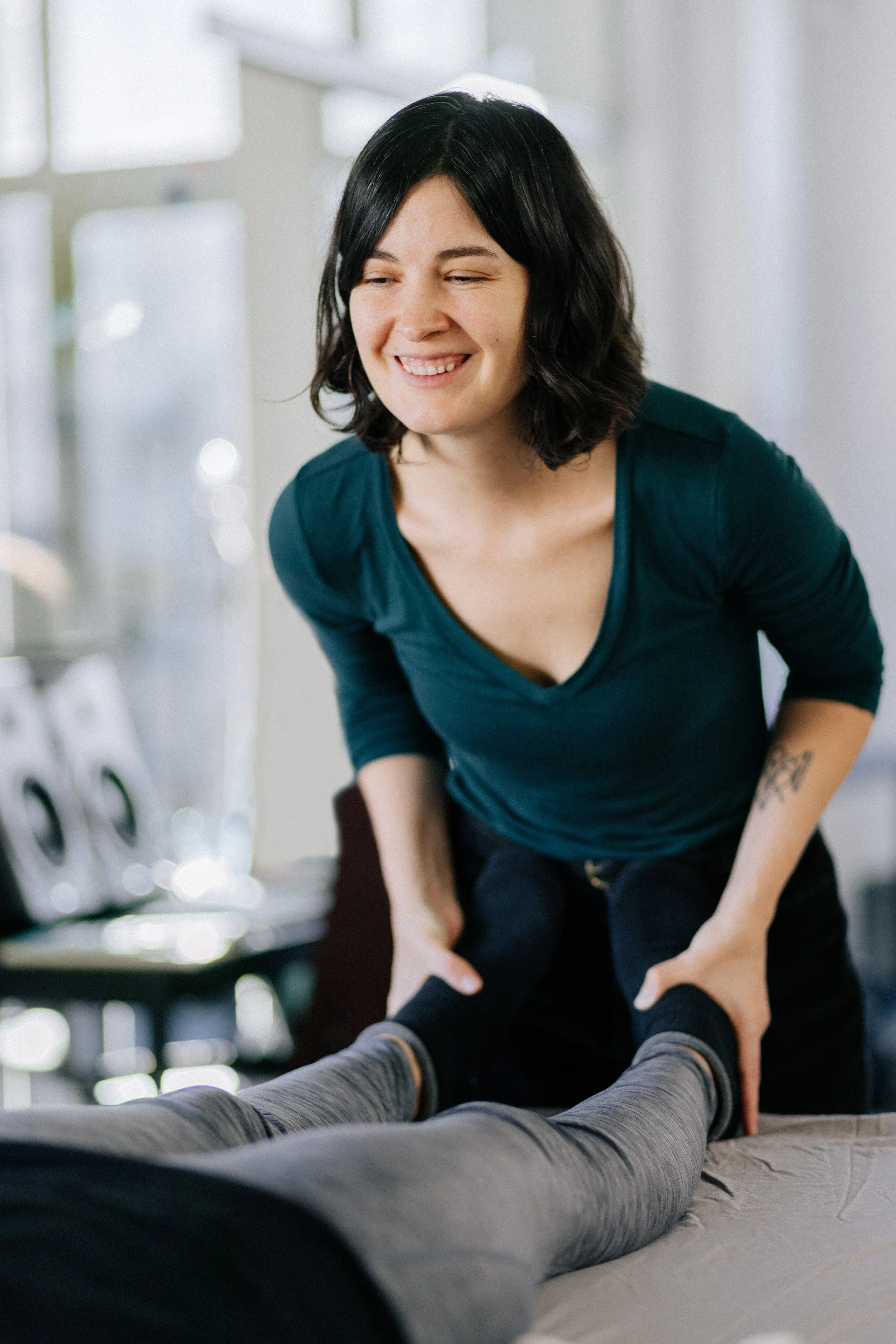 A woman giving a somatic bodywork session to a person lying on a massage table in a bright room.