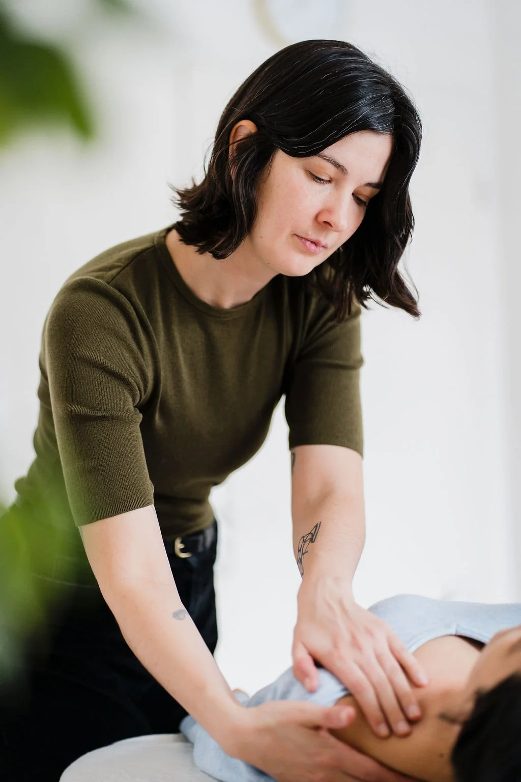 A woman giving a Pantarei Approach Bodywork session to someone lying down, focusing on the person's shoulder.