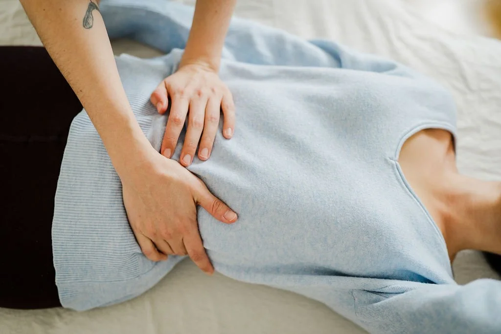 The Pantarei Practitioner has her hands on her client's stomach. The client is lying on a message table.