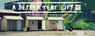 A billboard promoting a community called 'A Better Tent City' with small tents or shelters shown on the billboard and nearby structures.