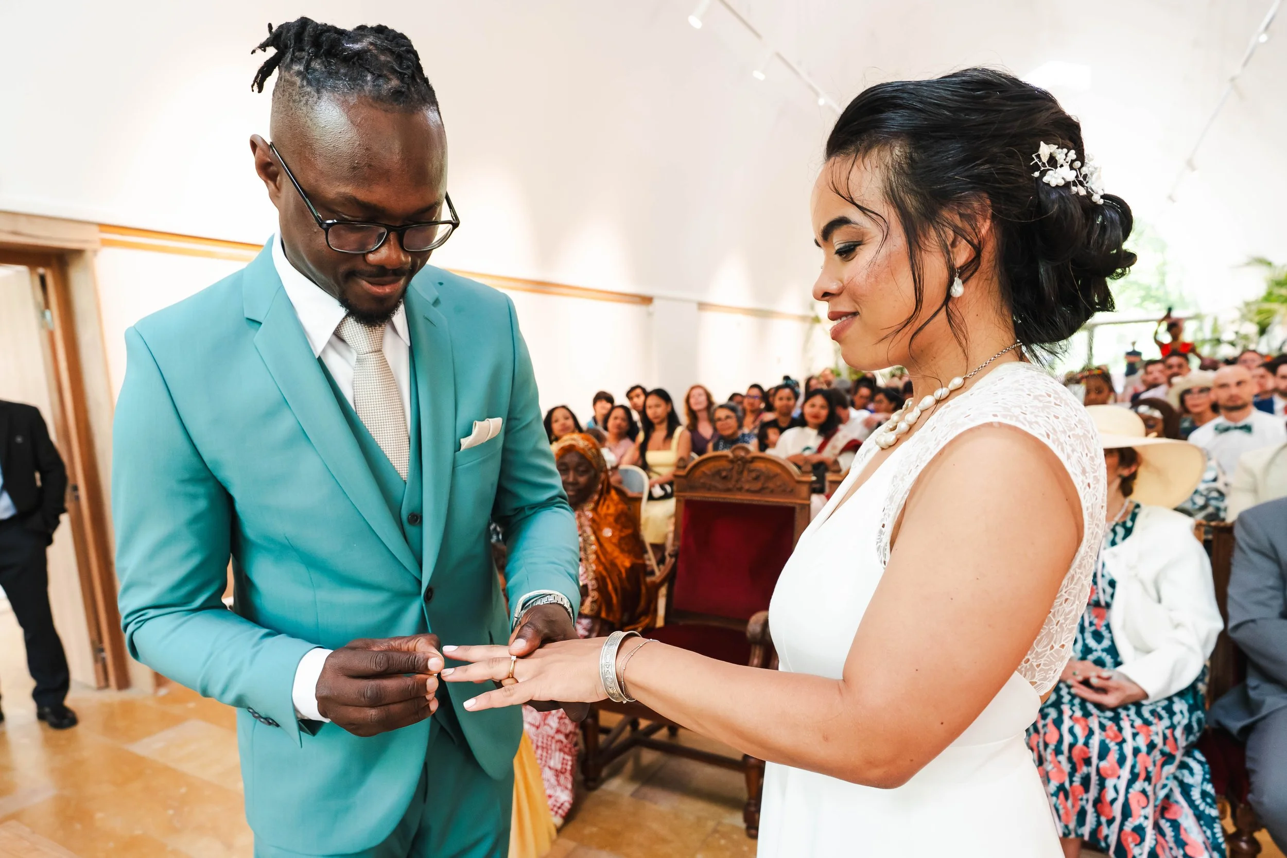 Un couple échange leurs bagues lors d'un mariage en intérieur dans la mairie XIIème, entouré d'invités .