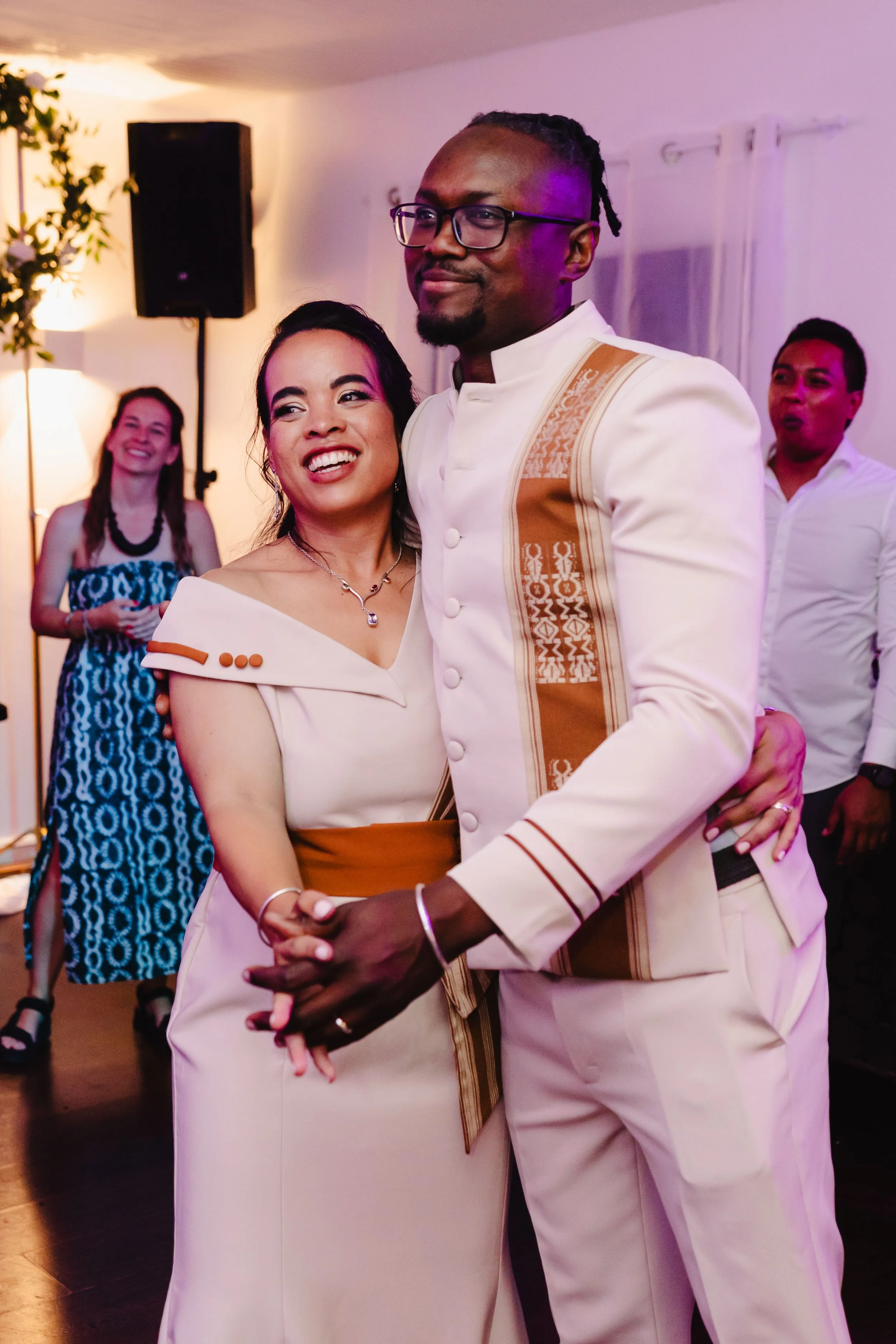 Un couple danse lors d'une célébration, entouré d'autres personnes, dans une pièce bien éclairée.