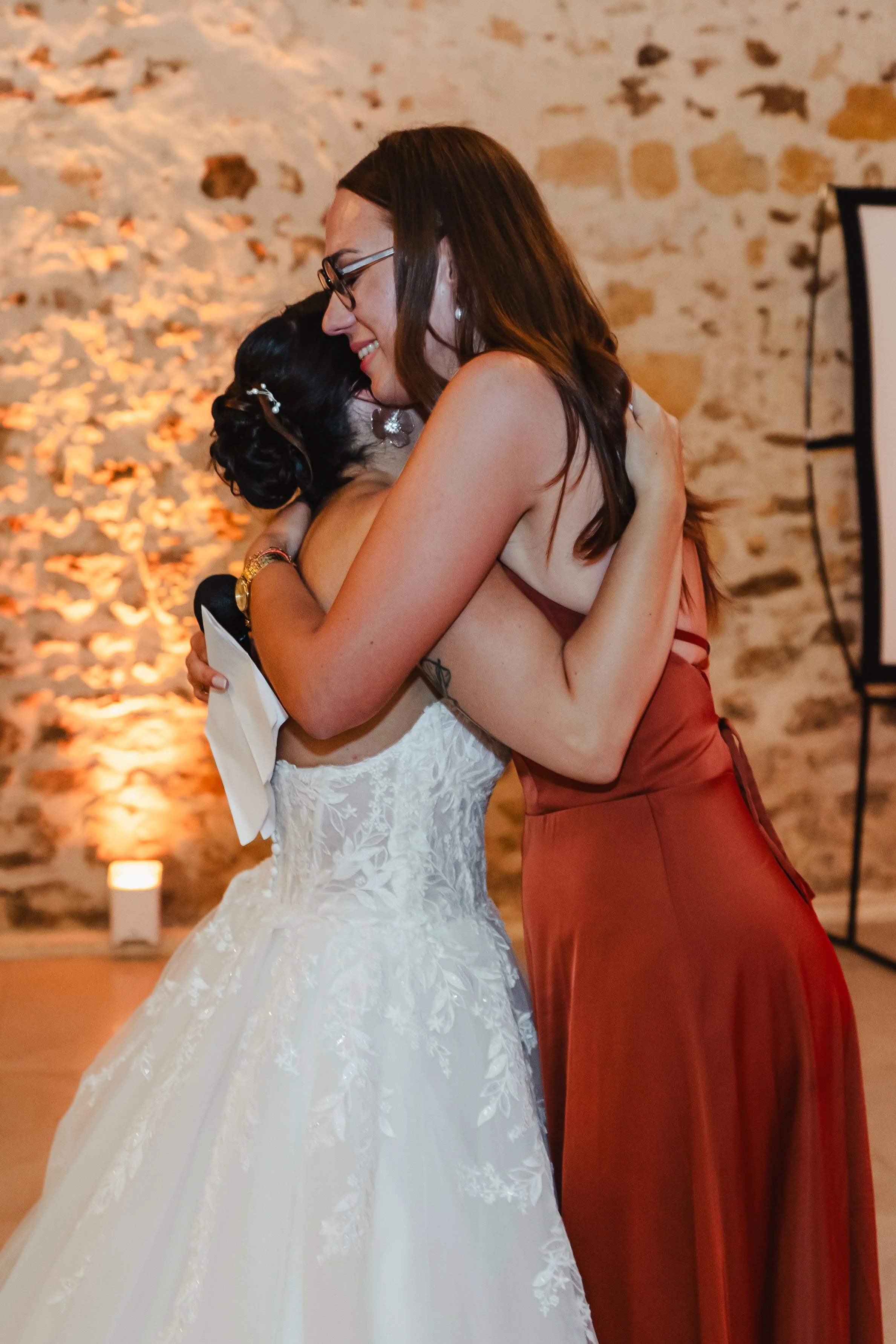 Deux femmes s'embrassent lors d'une fête, une en robe de mariée blanche et l'autre en robe rouge.